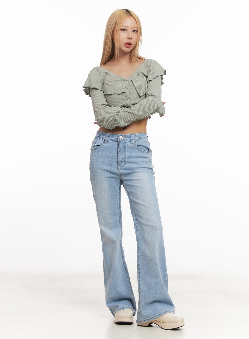 Suzy Slim-Fit Bootcut Jeans CM505 in light blue, full-body front shot on model with arms crossed, washed denim bootcut silhouette, paired with green ribbed ruffle crop top and platform clogs.