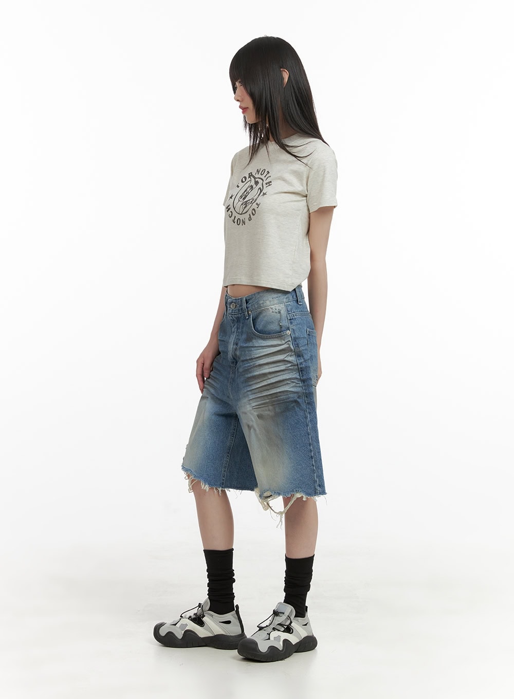 Destroyed Hem Bermuda Jorts CY414 in blue, side view on model, midi wide-fit washed denim showing faded whisker detailing and frayed hem, styled with beige crop tee and chunky sneakers.