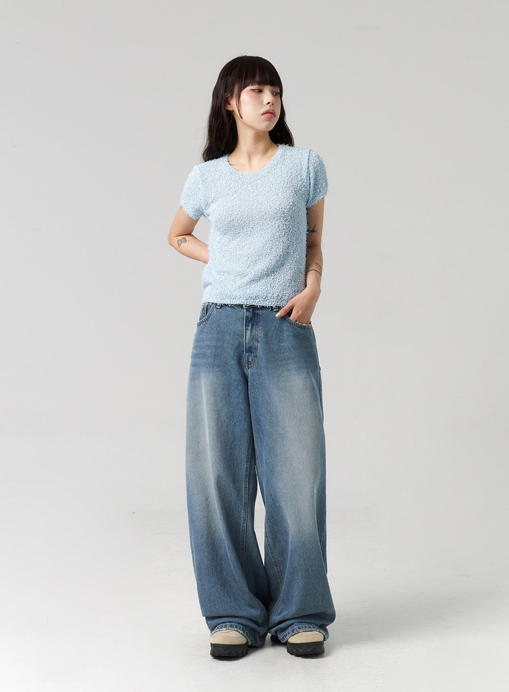 Baggy Jeans CL313 in washed blue, three-quarter front view on model turning slightly, extra-wide leg cotton denim with gradient fade, styled with light blue bouclé tee.
