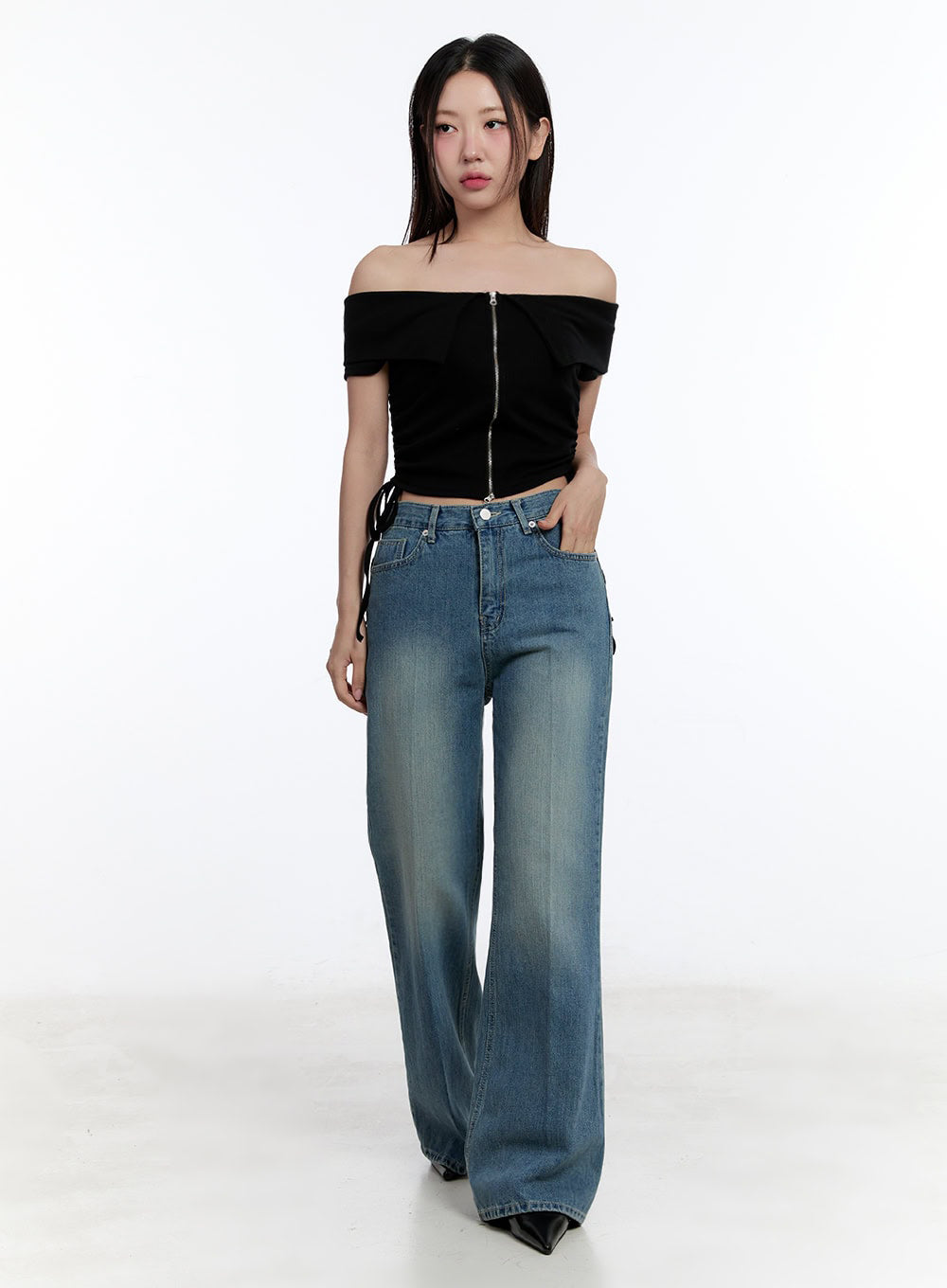 Aliya Washed Bootcut Jeans IU503 in dark blue, full-body front shot on model, relaxed wide fit with subtle bootcut flare, paired with black off-shoulder crop top, hand in pocket.