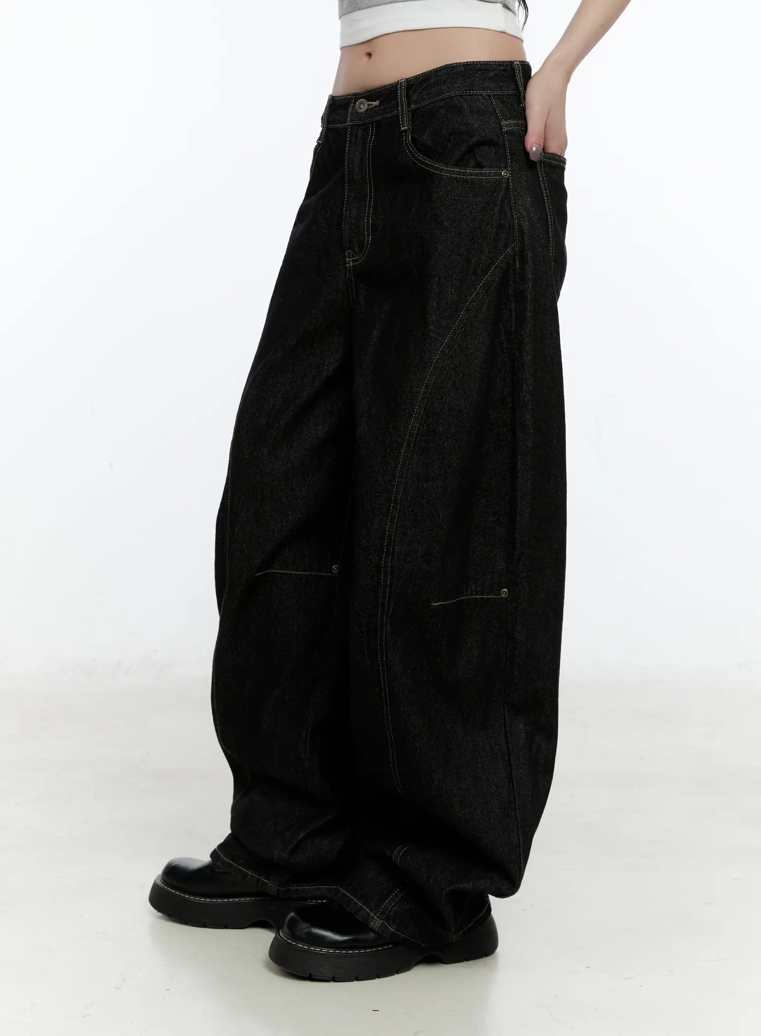 Maryam Low-Rise Dark-Washed Jeans CN517 in black, side view on model, wide-leg silhouette with visible contrast stitching and seam panels, low-rise fit, worn with black chunky loafers.