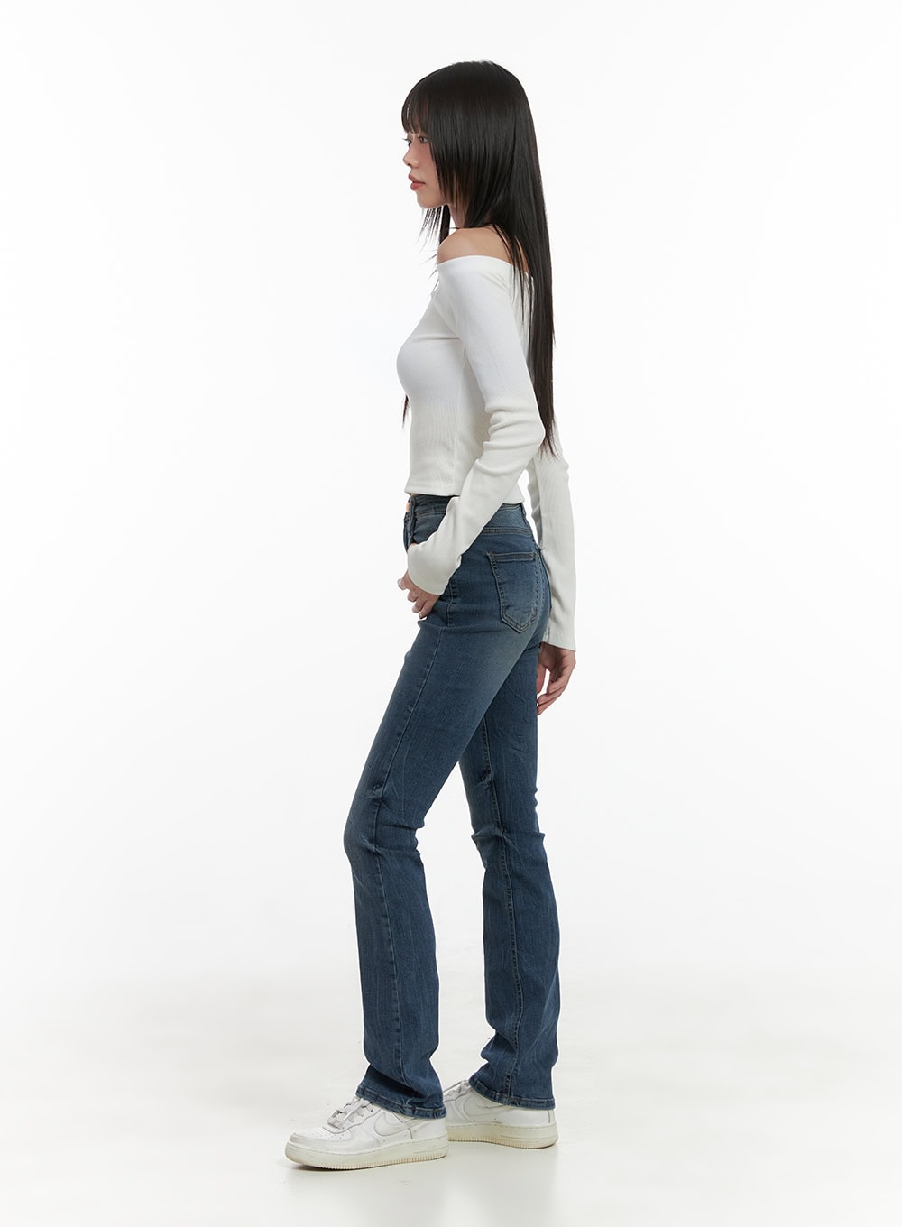 Pixie Slim Washed Bootcut Jeans CG427 in blue, side view on model, showing slim leg silhouette with subtle bootcut flare, high-rise waist, paired with white off-shoulder top and sneakers.
