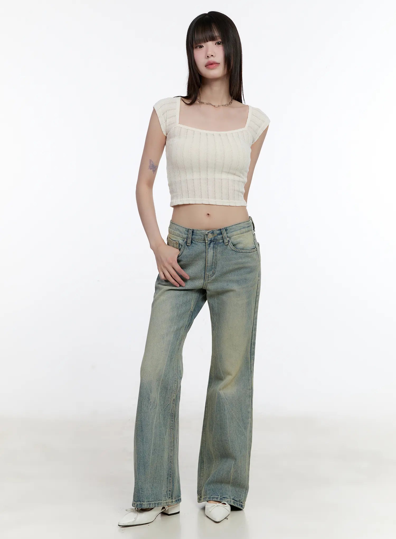 Roa Vintage Blue Flared Denim Jeans CL504 in blue, full-body front shot on model hand in pocket, low-rise washed bootcut denim, paired with cream square-neck knit crop top and white flats.