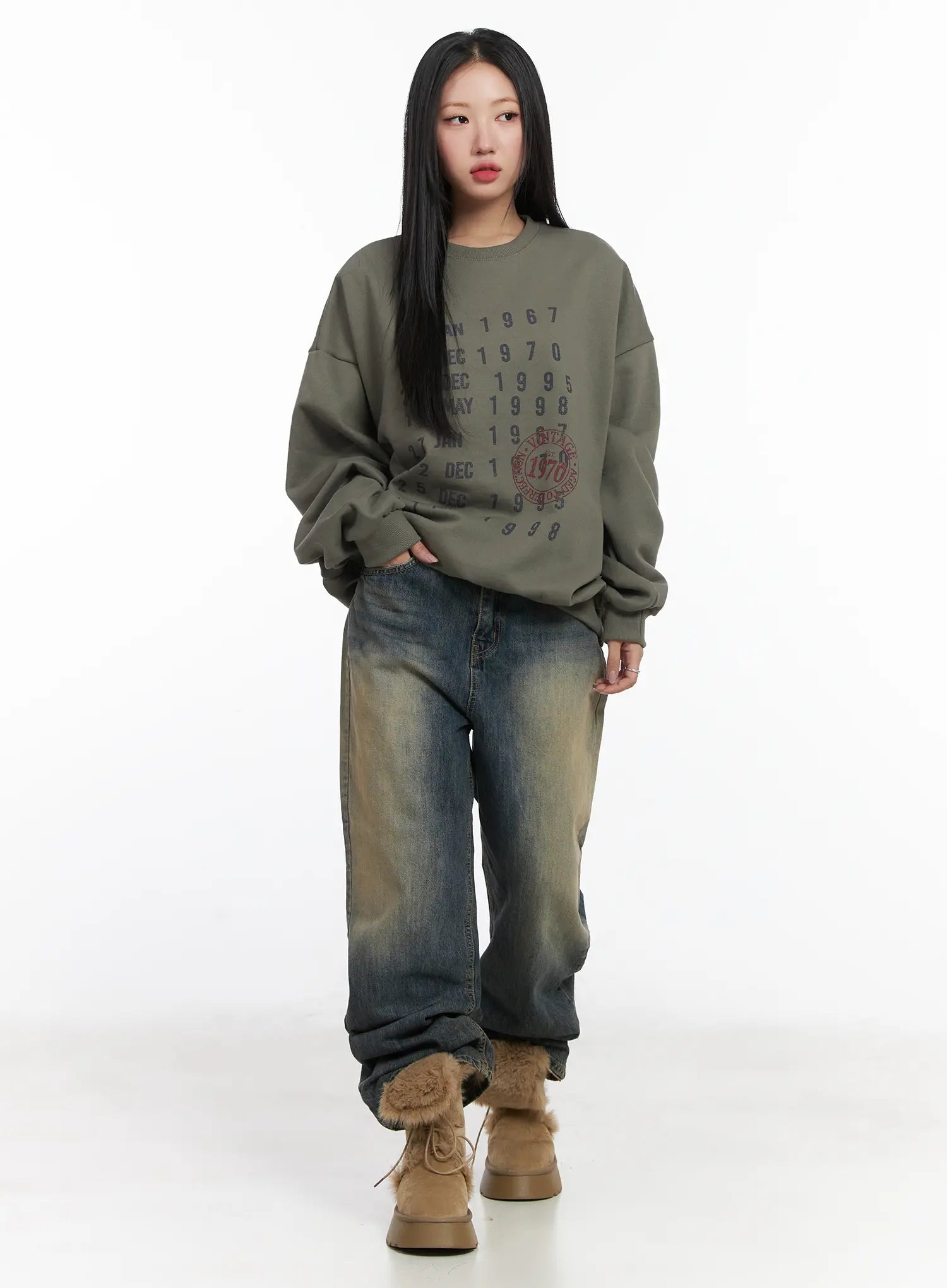 Wide Washed Jeans CS06 in vintage blue, full-length front view on model walking, wide-leg washed denim with yellow-toned fading, hand in pocket, paired with olive graphic sweatshirt and fur boots.