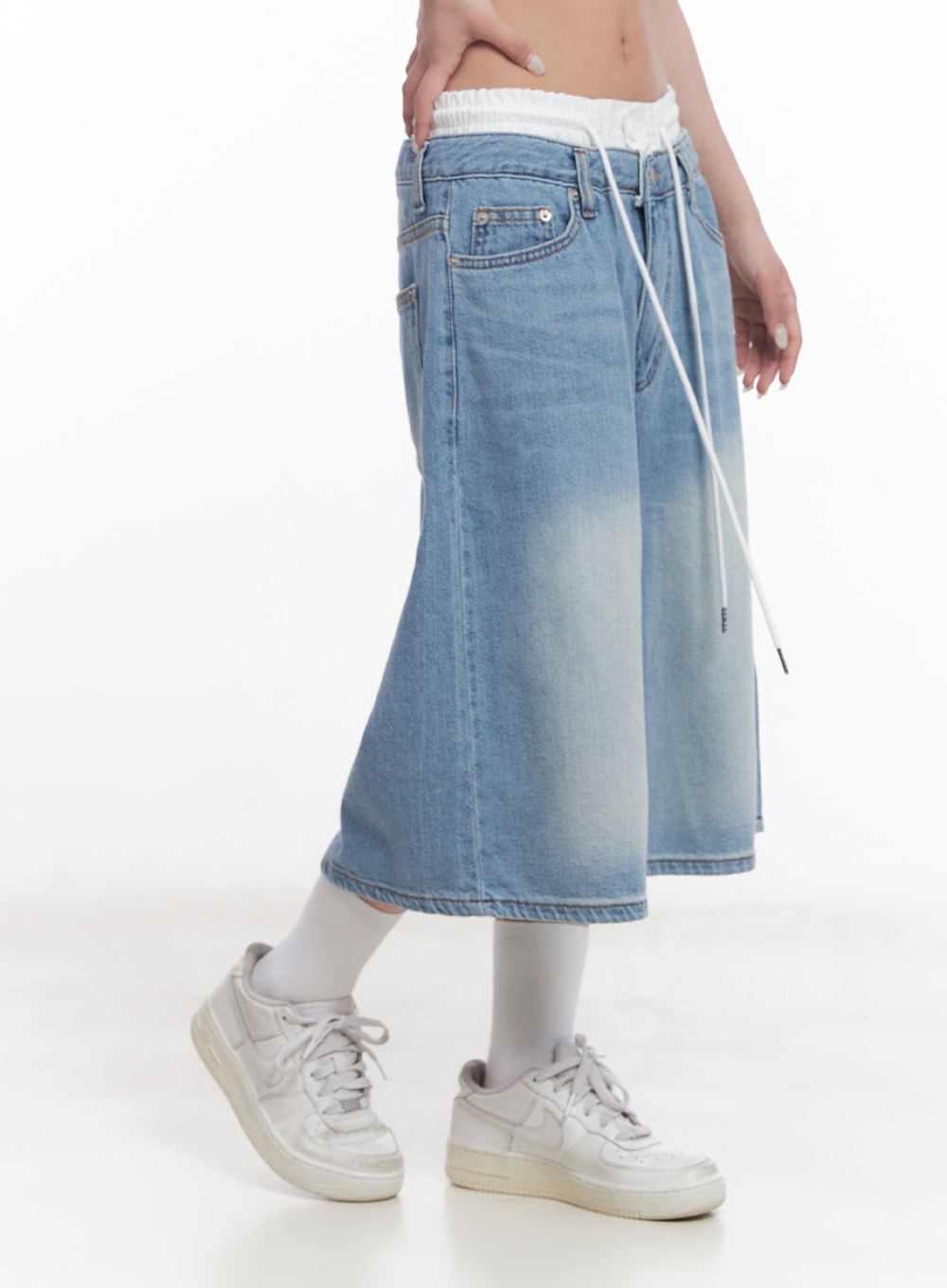 Layered Drawstring Baggy Jorts CY527 in light blue, side view on model, low-waist washed denim with white ruched inner waistband and long drawstring, wide baggy midi silhouette, styled with white sneakers.