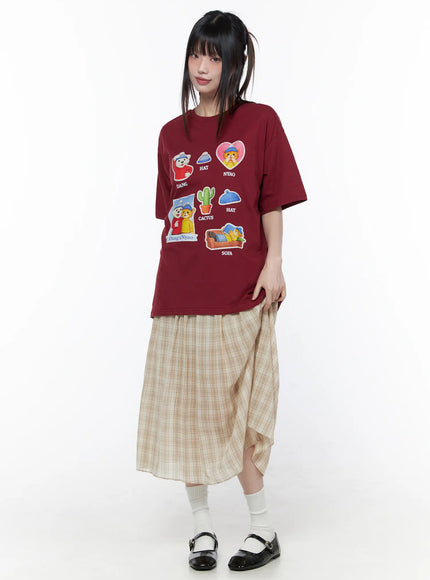 Oversized Graphic Print Tee CU519 in dark red, full-length front view on model, boxy cotton short sleeve with Dang & Nyao graphic prints, styled with plaid skirt, white socks, and black Mary Jane shoes.