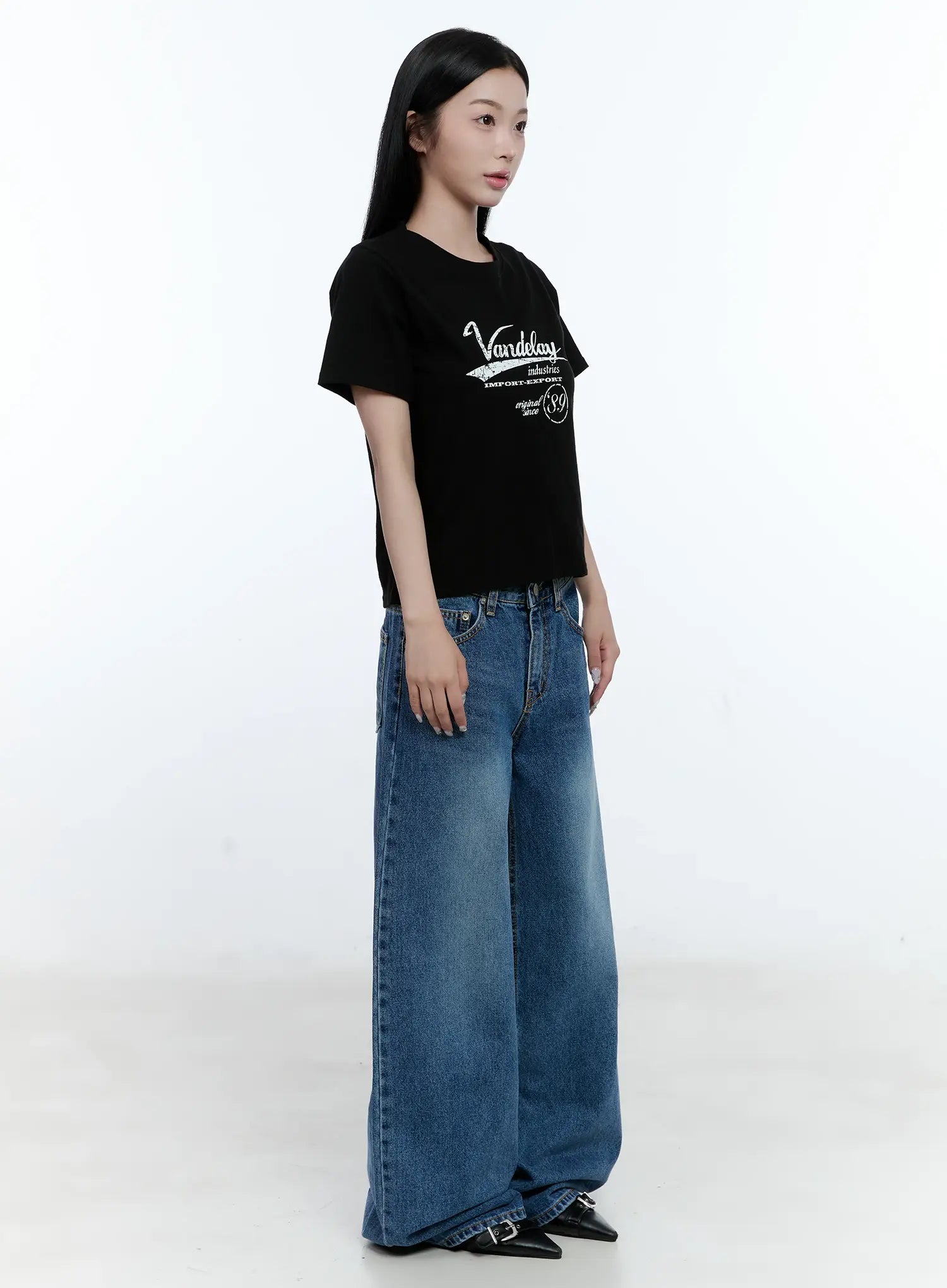 Dahye Washed Relaxed-Fit Denim Jeans CL530 in blue, three-quarter front side view on model, wide-leg relaxed fit with washed finish, paired with black graphic crop tee and black buckle heels.
