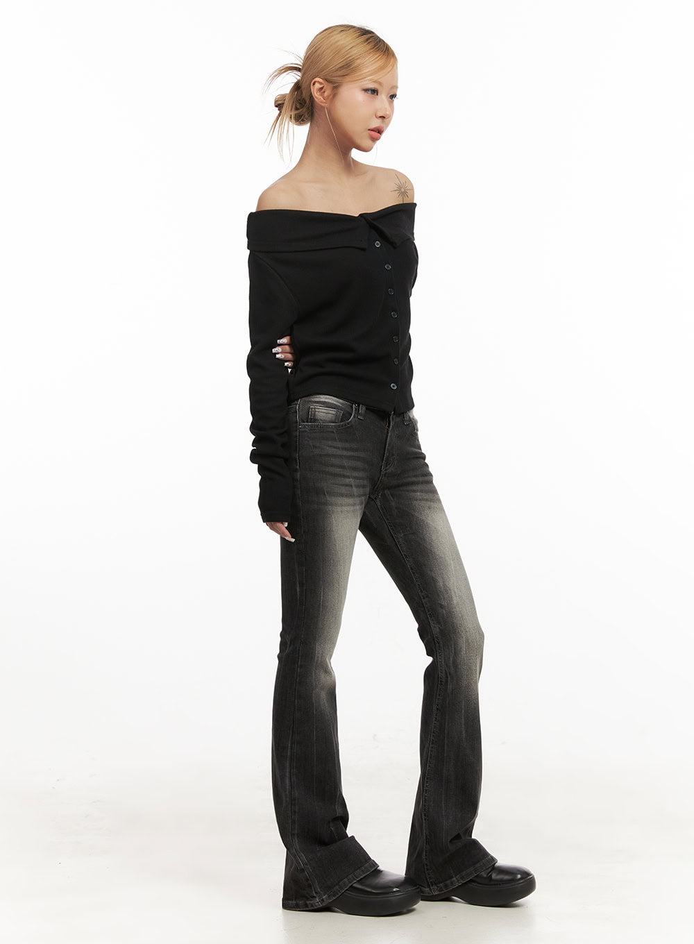 Georgina Low-Rise Flared Jeans CJ507 in black, 3/4 side view on model, washed denim with vintage fading, low-rise fit hugging hips and flaring at ankle, paired with black off-shoulder cardigan.