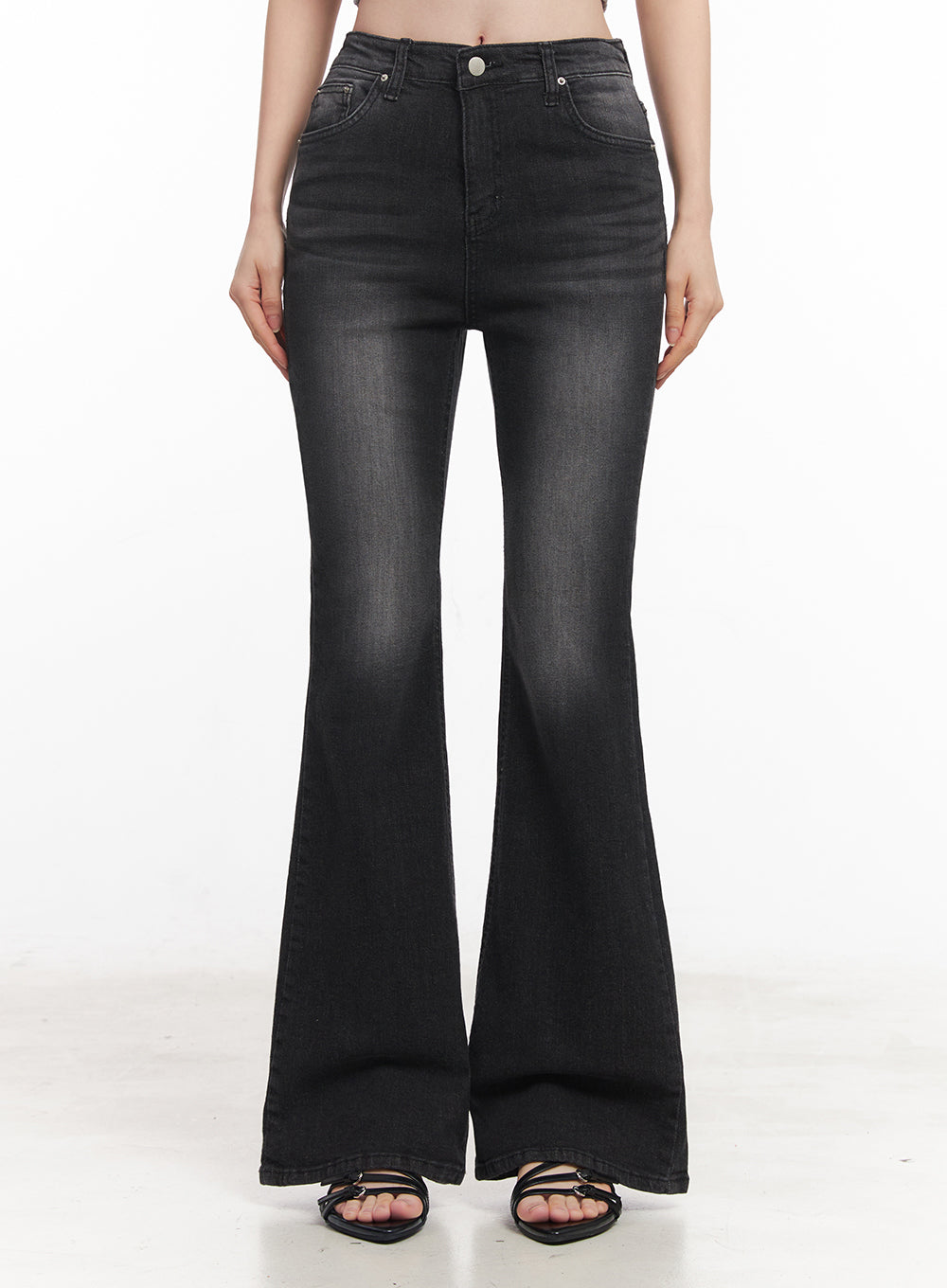 Lior Slim-Fit Bootcut Jeans IY516 in black, front lower-body shot on model, slim-fit washed denim with gentle bootcut flare from knee, high-rise waist, black strappy sandals.