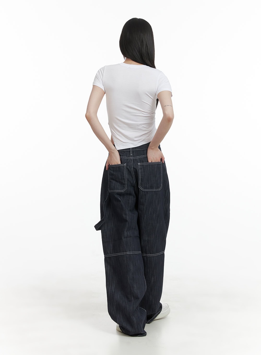 Low-Rise Strap Baggy Jeans CY414 in dark blue, back view on model revealing large patch pockets with contrast white stitching, worn with white crop tee and sneakers.