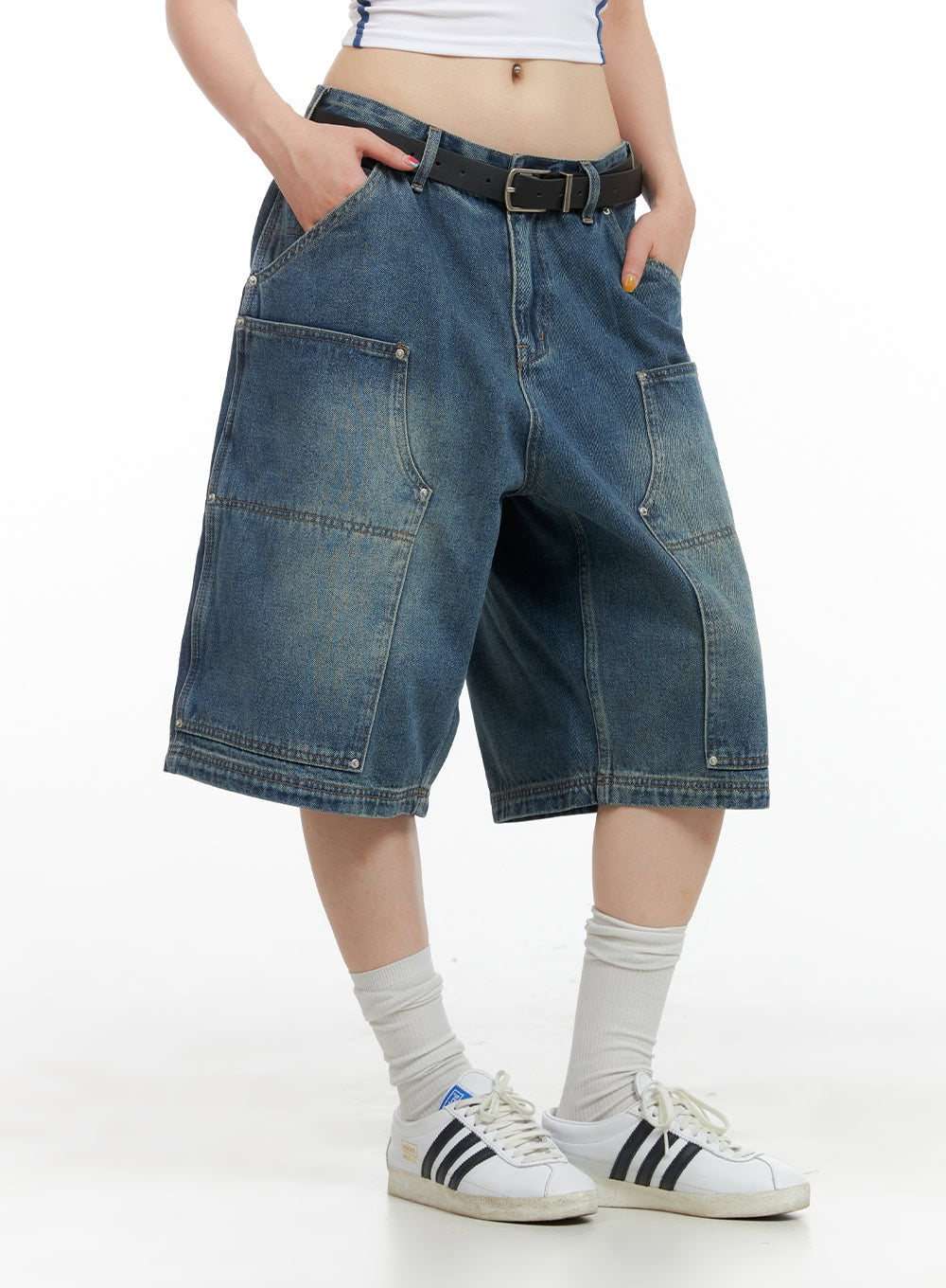 Stud Washed Baggy Jorts (UNISEX) CG408 in blue, side-front view on model, wide-fit washed denim with stud-accented panels and stitching, belted waist, paired with white sneakers.