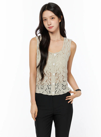 Crochet Knit Sleeveless Top CU522 in beige, front three-quarter view on model, scoop neckline and white button placket, open-knit lace detail, paired with black trousers.