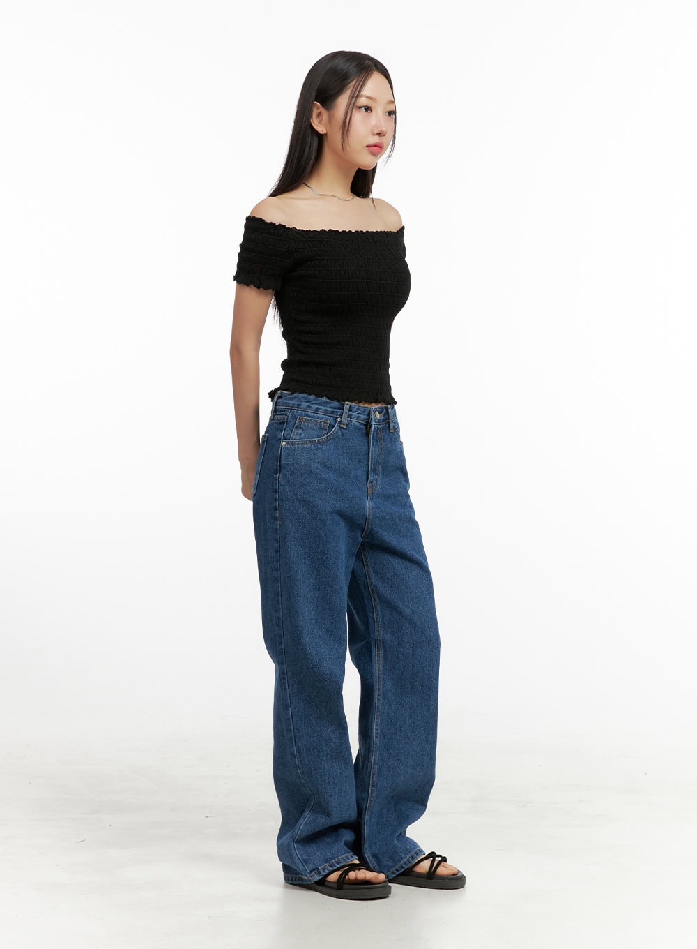 Blue Wide-Leg Jeans OU407 in blue, side full-body view on model, wide-fit washed denim showing high waist and floor-grazing wide leg silhouette, paired with black off-shoulder top and sandals.