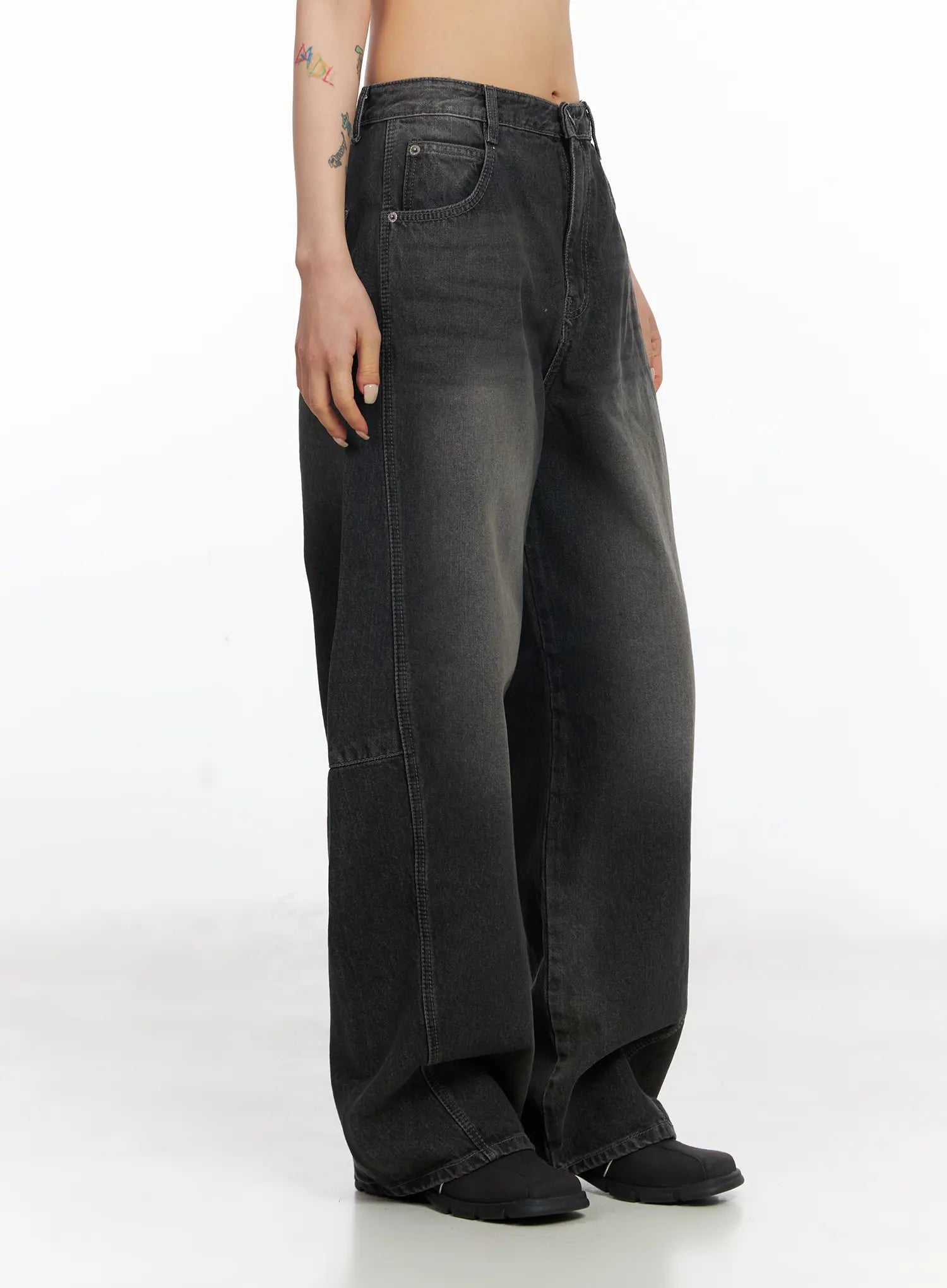 Nayeli Baggy Jeans CJ522 in dark gray, side view waist-down on model, washed wide-fit cotton denim showing curved seam panel and back pocket, with black boots.