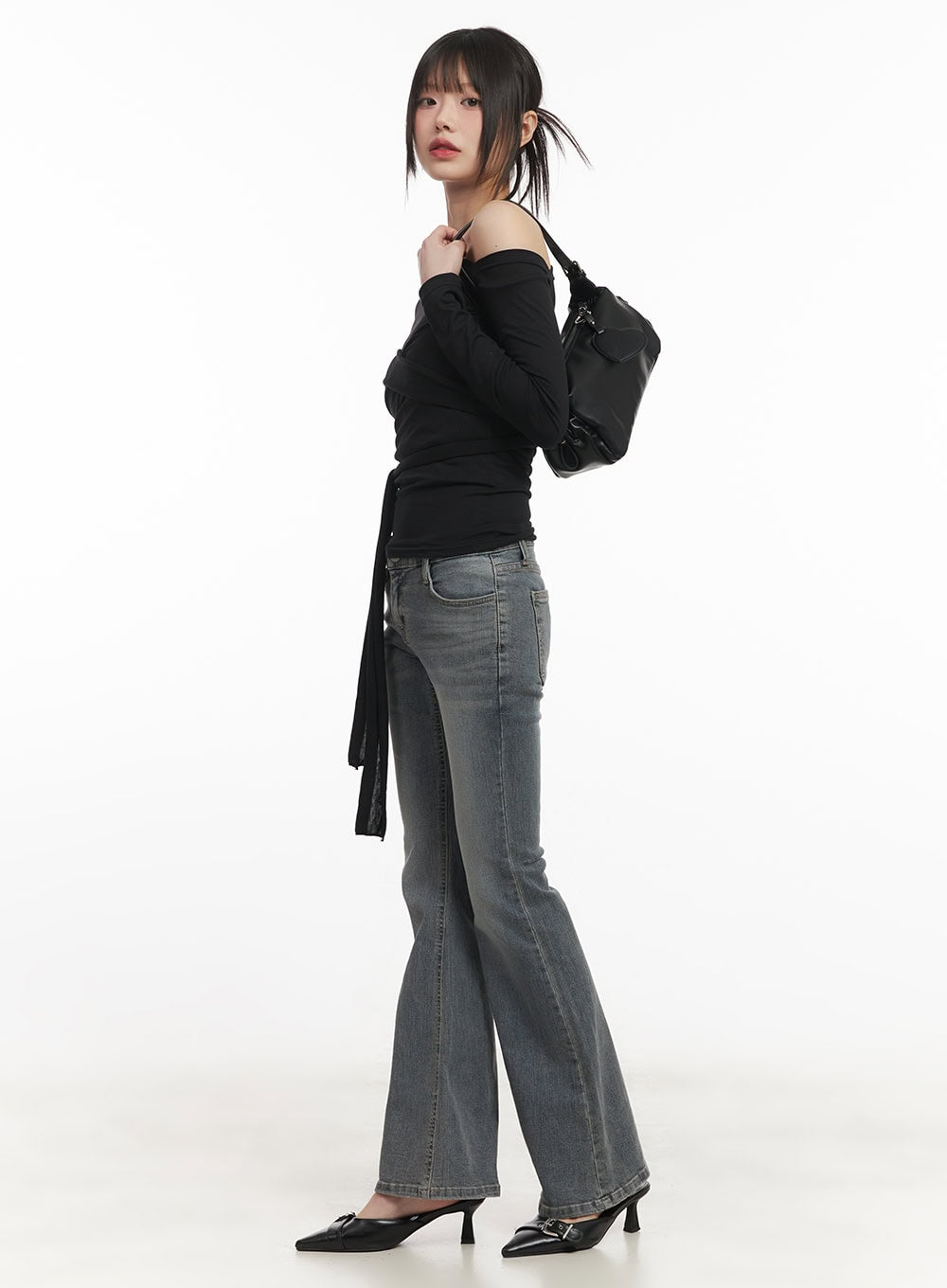 Rachel Washed Bootcut Jeans with Hip Pads CF518 in gray, side full-body editorial shot on model, low-waist bootcut flare styled with black tie top and black shoulder bag.