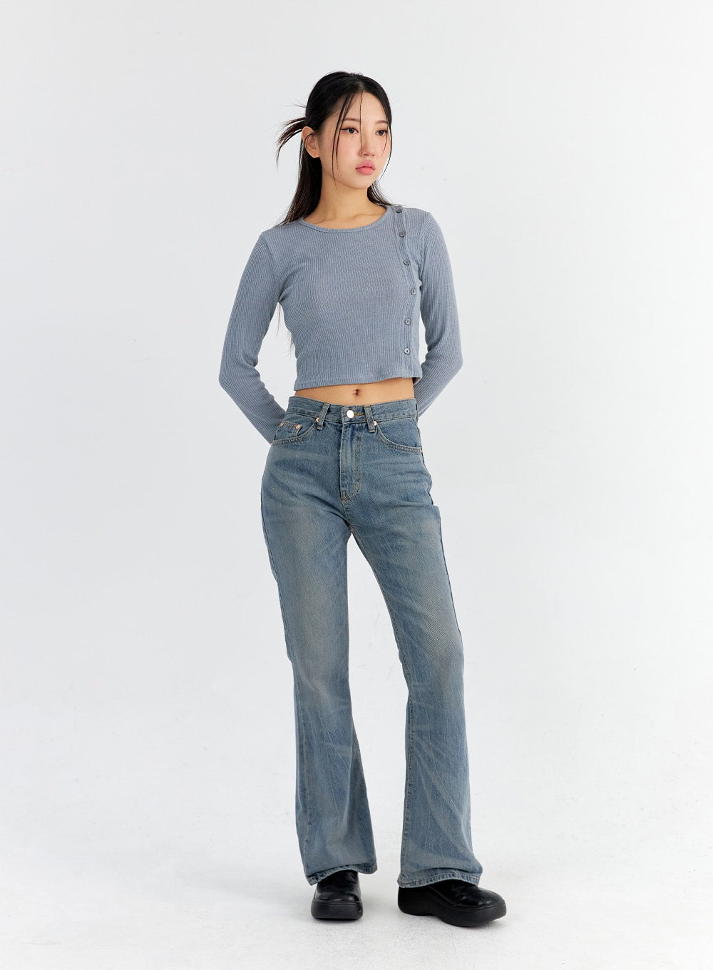 Vintage Washed Bootcut Jeans CO325 in blue, full-body slight front-angle on model with hands in pockets, slim fit vintage-washed denim, bootcut flare from knee, paired with grey crop top.