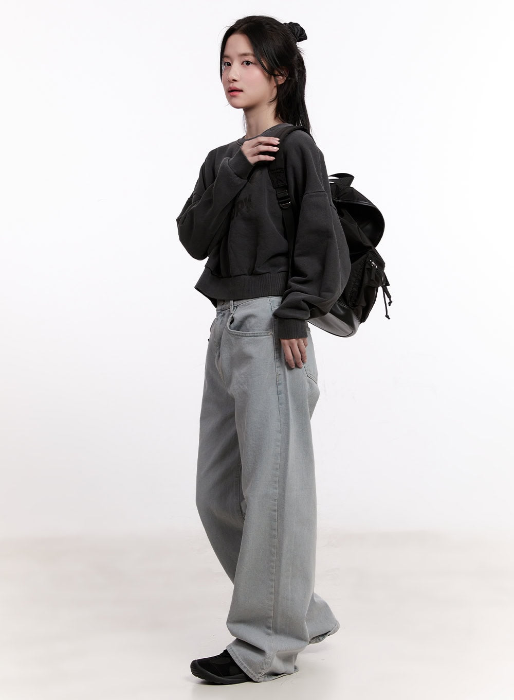 Casey Washed Baggy Wide-Leg Jeans CM526 in light gray, three-quarter side shot on model, wide-leg washed denim styled with dark crop sweatshirt and large black backpack, casual street look.