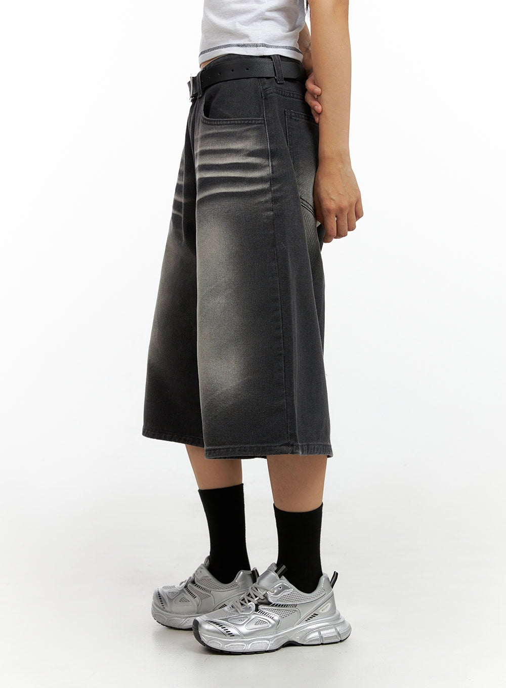 Washed Baggy Jorts IL419 in black, side close-up on model, wide-fit midi denim showing faded wash texture, belt loops, and oversized leg silhouette with silver chunky sneakers.
