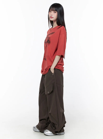Wide Leg Pintuck Cargo Pants CU519 in dark brown, side view on model, cargo snap pocket and diagonal pintuck seams visible, styled with red graphic tee and silver sneakers.