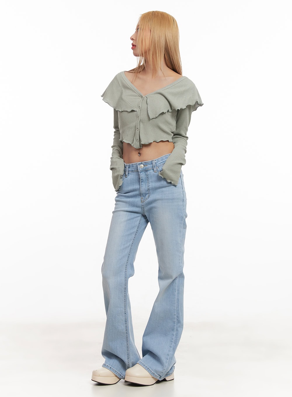 Suzy Slim-Fit Bootcut Jeans CM505 in light blue, three-quarter side view on model looking back, slim-fit washed denim flare, paired with sage green ruffle crop cardigan and white clogs.