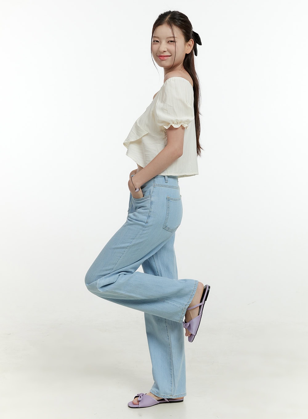 Ava Light Washed Straight Jeans OL430 in light blue, side view on model with leg raised, wide straight-leg silhouette, high-rise waist, light washed denim, paired with cream crop top and lavender sandals.
