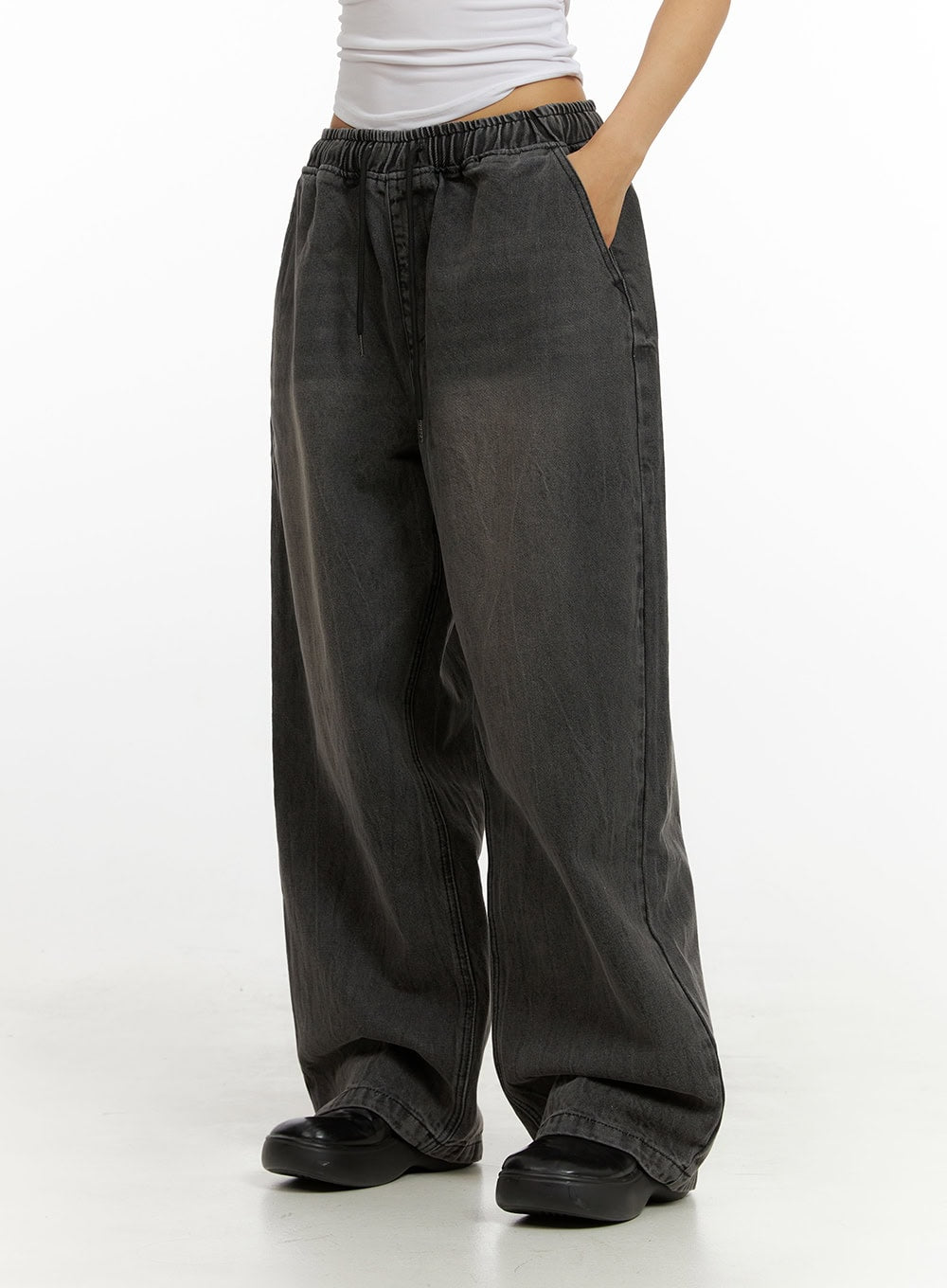 Banding Baggy Jeans IU412 in washed black, side close-up on model, elastic banded waistband and drawstring detail visible, wide-leg washed cotton denim silhouette, paired with white crop top.