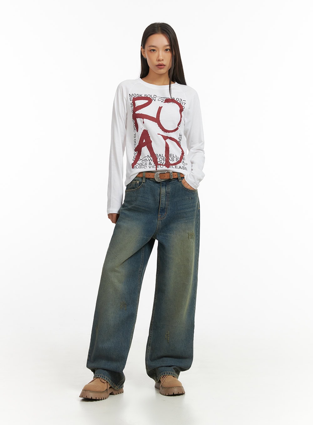 Anya Wide Fit Denim Jeans IO409 in blue, full front standing view on model, wide-fit washed denim with faded vintage tones and subtle distressing, styled with white graphic long-sleeve and brown western belt.