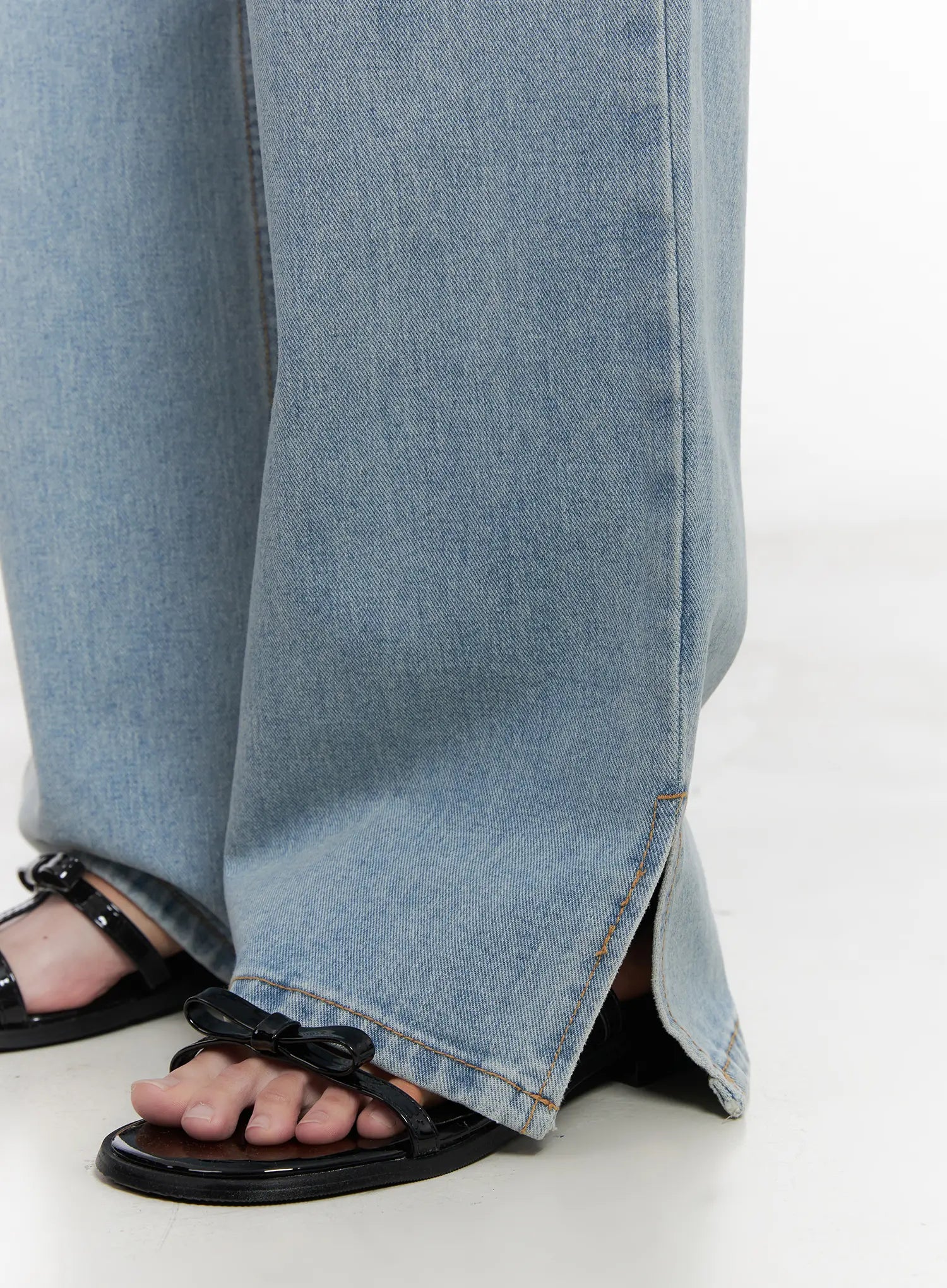 Hyuna Slit Straight-Fit Jeans CU525 in light blue, close-up detail of hem slit on model, showing front-seam stitching and open hem slit, worn with black bow-detail sandals.