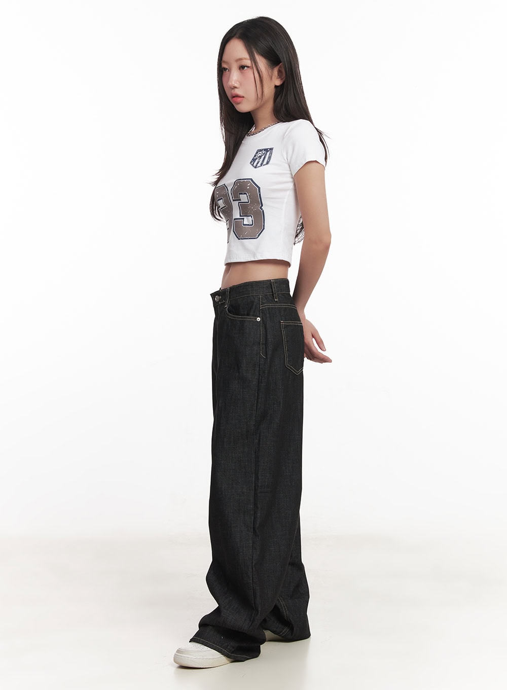 Fenna Baggy Jeans CA529 in black, side view on model, showing low-rise waistband, contrast topstitching, and extreme wide-leg silhouette with white sneakers.