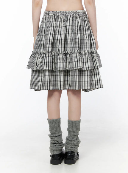 Plaid Layered Midi Skirt CU519 in black, back view on model, elastic smocked waistband and double ruffle tiers visible, black-white plaid, paired with grey leg warmers and loafers.