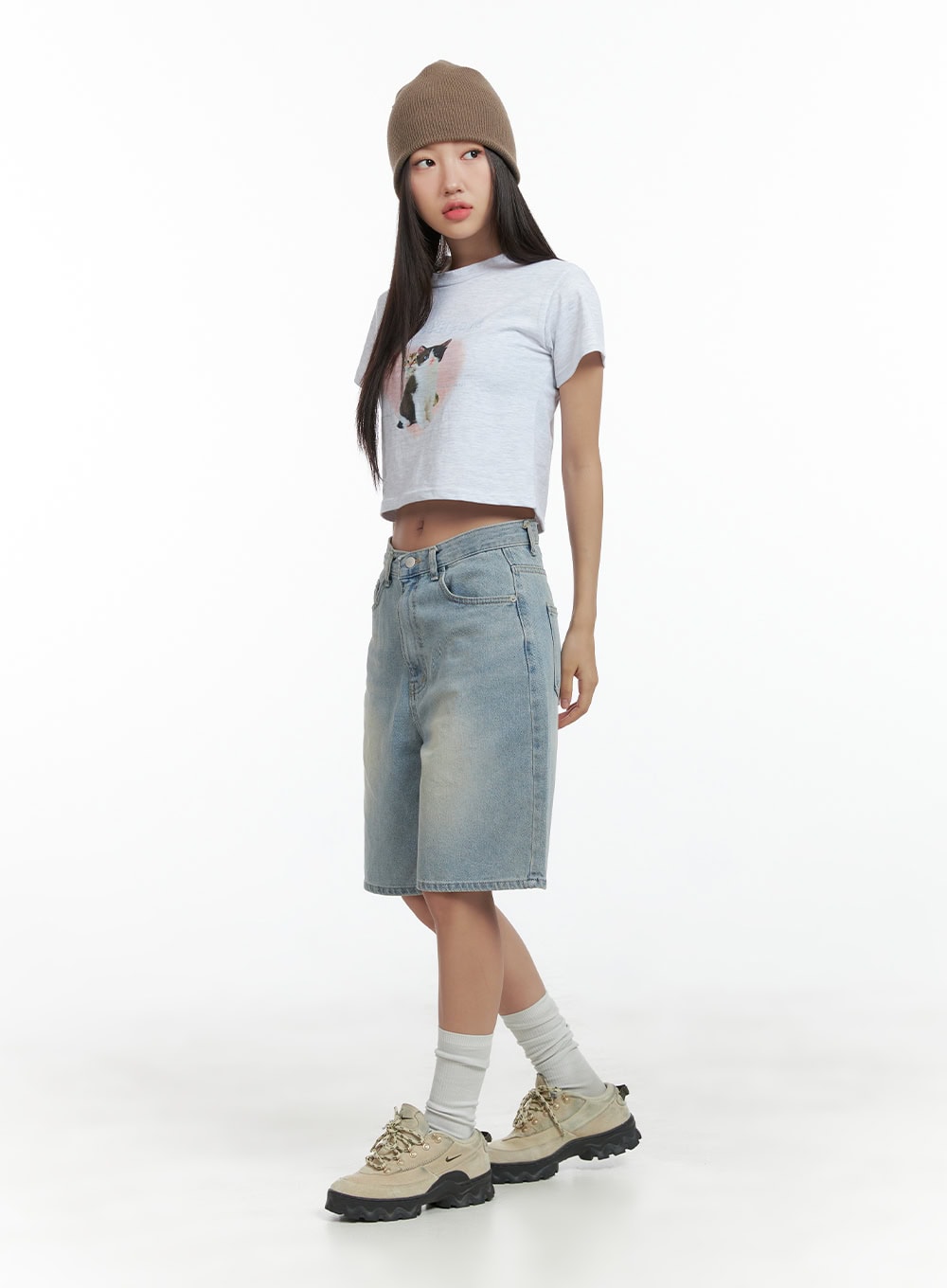 Light Washed Jorts CL417 in light blue, full-body side shot on model with beanie and cat graphic crop tee, wide-fit light washed denim shorts with knee-length cut, street style look.