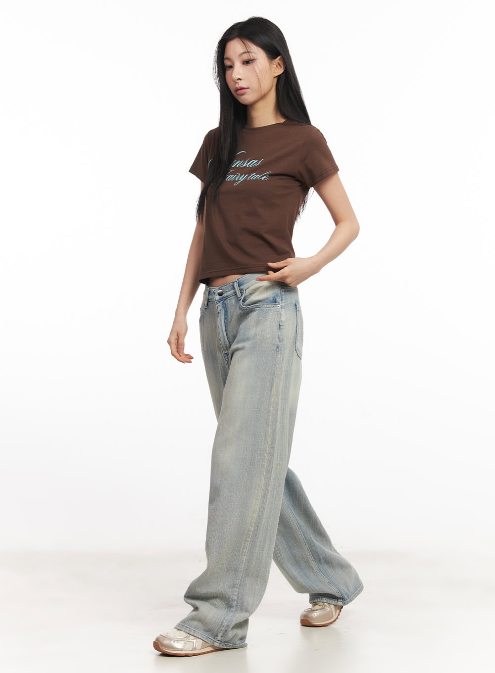 Jessi Washed Wide-Leg Jeans CA514 in light blue, three-quarter front view on model mid-stride, washed cotton denim with relaxed wide fit, styled with brown crop tee and silver sneakers.