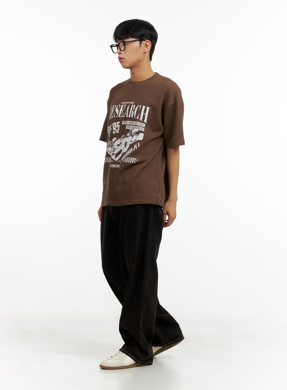 Men's Wide Fit Washed Baggy Jeans CL429 in Black, three-quarter side view on male model, oversized baggy leg with contrast topstitching, worn with brown graphic tee and white sneakers.