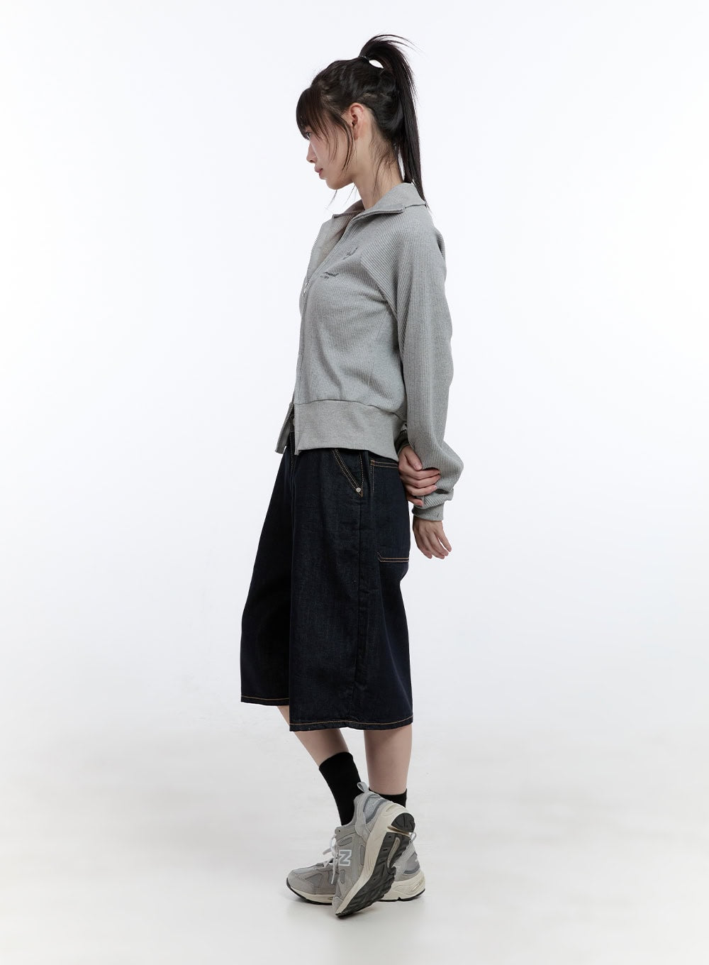 Dora Stitched Baggy Jorts CG413 in dark blue, side profile full-body shot on model, knee-length wide denim with visible contrast topstitch hem, paired with grey zip sweatshirt.