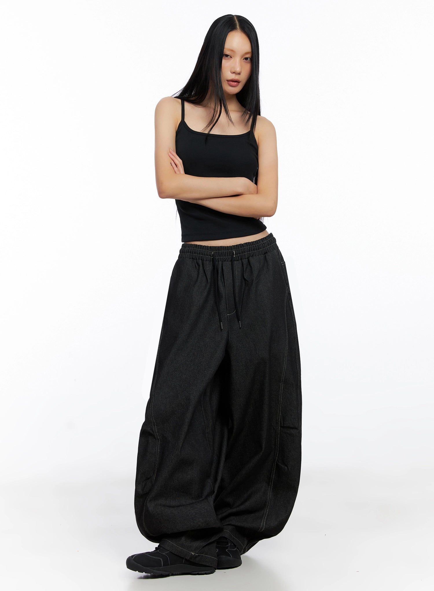 Ayra Graphic Baggy Jeans IO516 in Black, front full-body on model arms crossed, long baggy cotton denim, elastic waist with drawstring, paired with black spaghetti-strap cami.