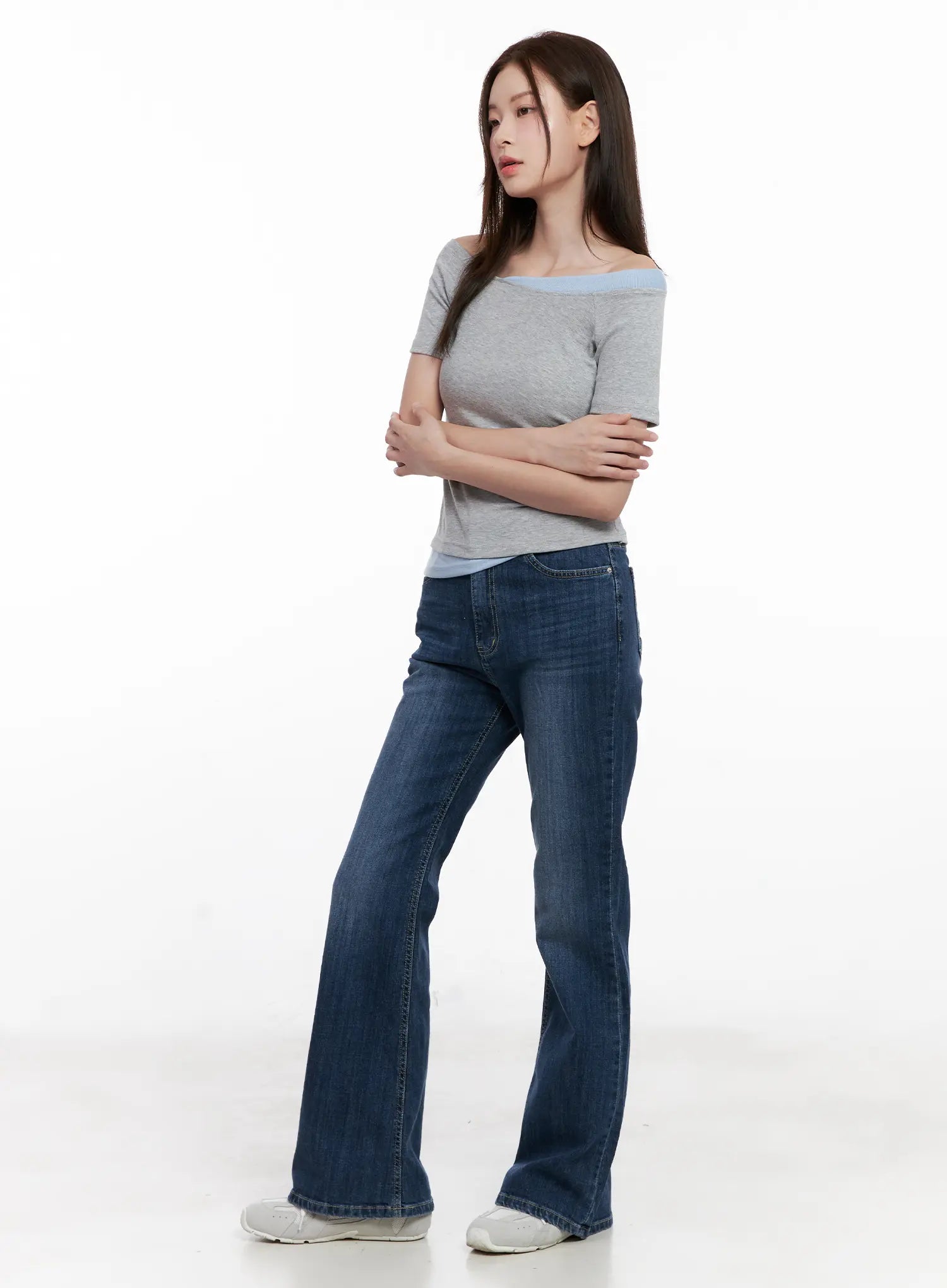Solhee Classic Flare Denim Jeans CL524 in dark blue, three-quarter side shot on model with arms crossed, flare bootcut length, styled with grey off-shoulder top.