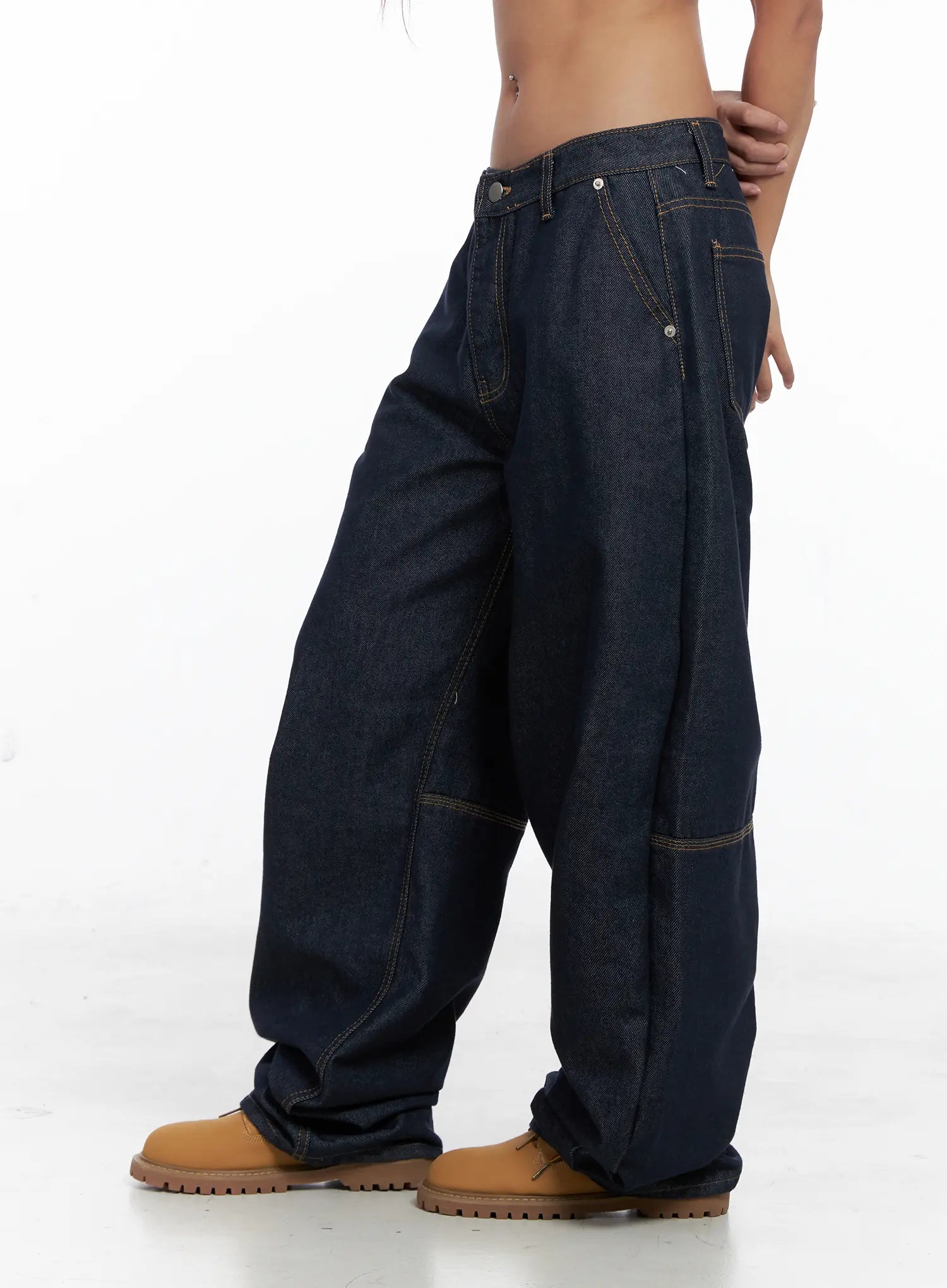 Relaxed Fit Dark Denim Jeans CS522 in dark blue, side view on model, exaggerated wide-leg balloon silhouette, contrast stitching and side carpenter pocket, stacked hem over tan boots.