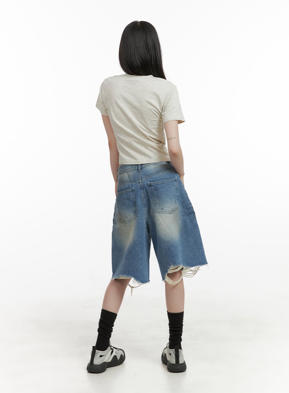 Destroyed Hem Bermuda Jorts CY414 in blue, full-body back view on model, wide-fit washed denim with dual back pockets and heavily destroyed raw hem, paired with beige crop tee and black socks.