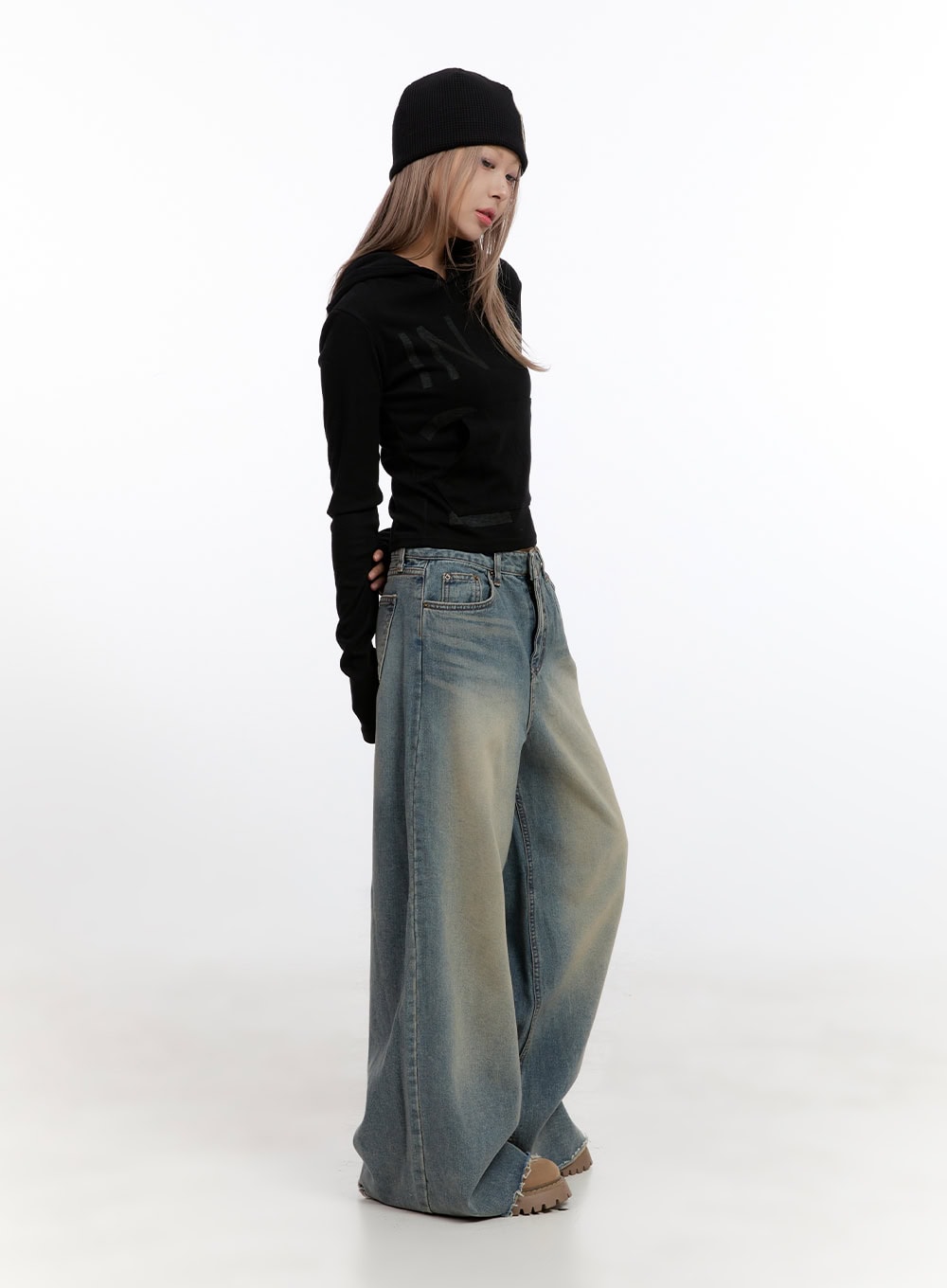 Felicia Cotton Wide Fit Baggy Jeans CN425 in blue, angled side view on model looking down, washed baggy denim, low-rise waistband, voluminous leg, frayed hem, styled with black cropped hoodie and beanie.