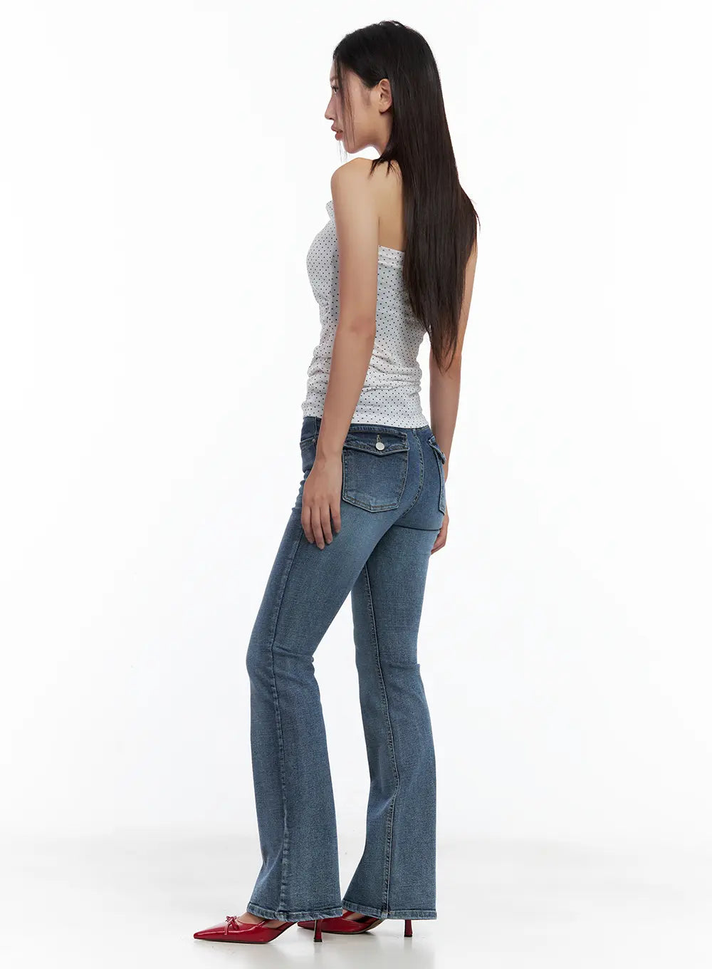 Beni Washed Flared Denim Jeans CL508 in dark blue, side view on model, flared hem and back pocket detail visible, styled with polka-dot halter top and red heels.