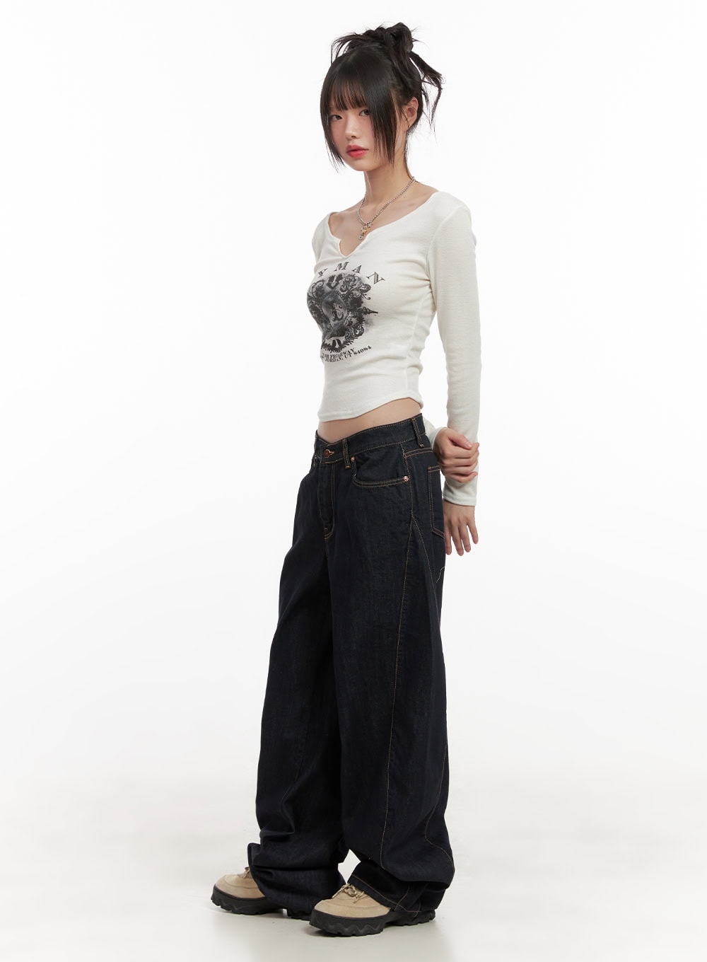 Fernanda Balloon-Fit Baggy Jeans CJ502 in dark blue, three-quarter side full-body shot on model, low-waist wide-fit denim with contrast stitch seams, paired with white graphic crop top and chunky sneakers.