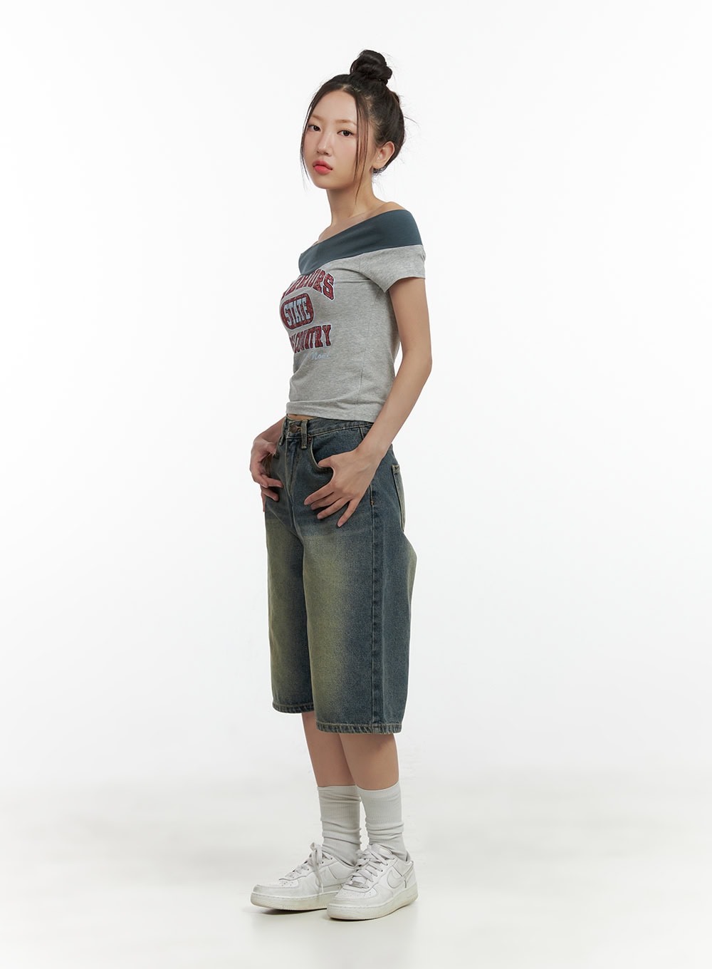 Slim Fit Bermuda Jorts CL410 in blue, three-quarter side shot on model, wide-leg washed denim with yellow-tinted fade, paired with grey off-shoulder top and sneakers.