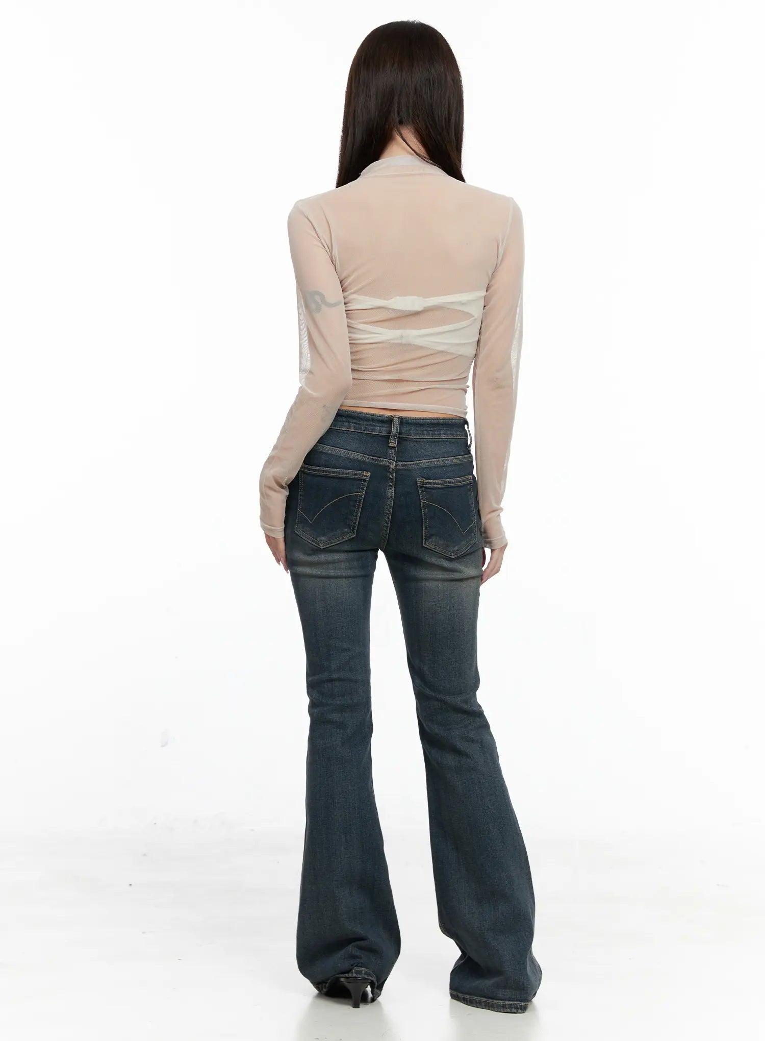 Rosé Washed Bootcut Jeans CO520 in dark blue, back full-length view on model, curved back pockets with topstitching, flared bootcut hem, worn with sheer top and black heels.