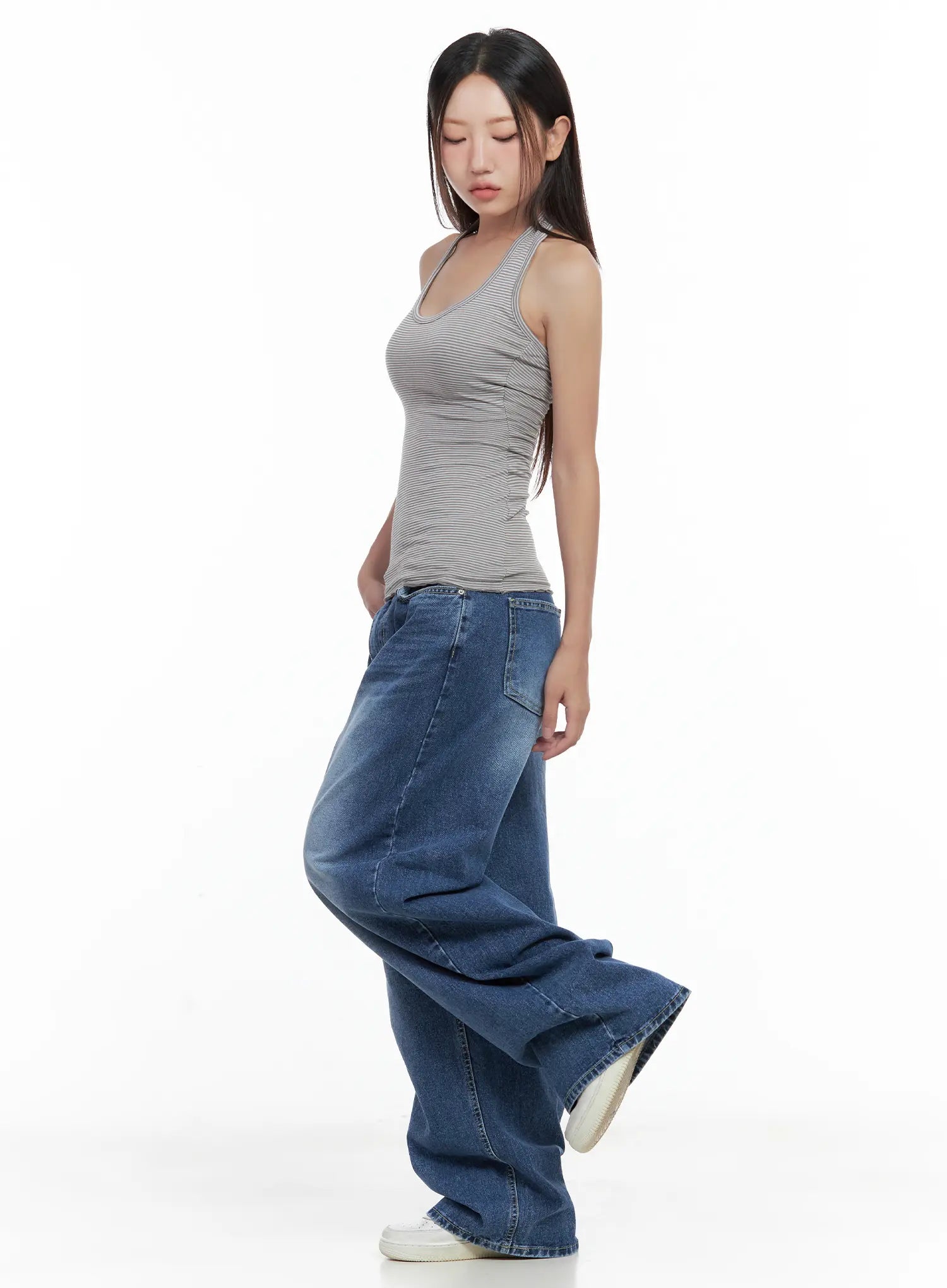 Hayoung Washed Wide-Leg Denim Jeans CL509 in dark blue, side view on model looking down, ultra-wide pooling leg silhouette, paired with grey striped halter tank and white sneakers.