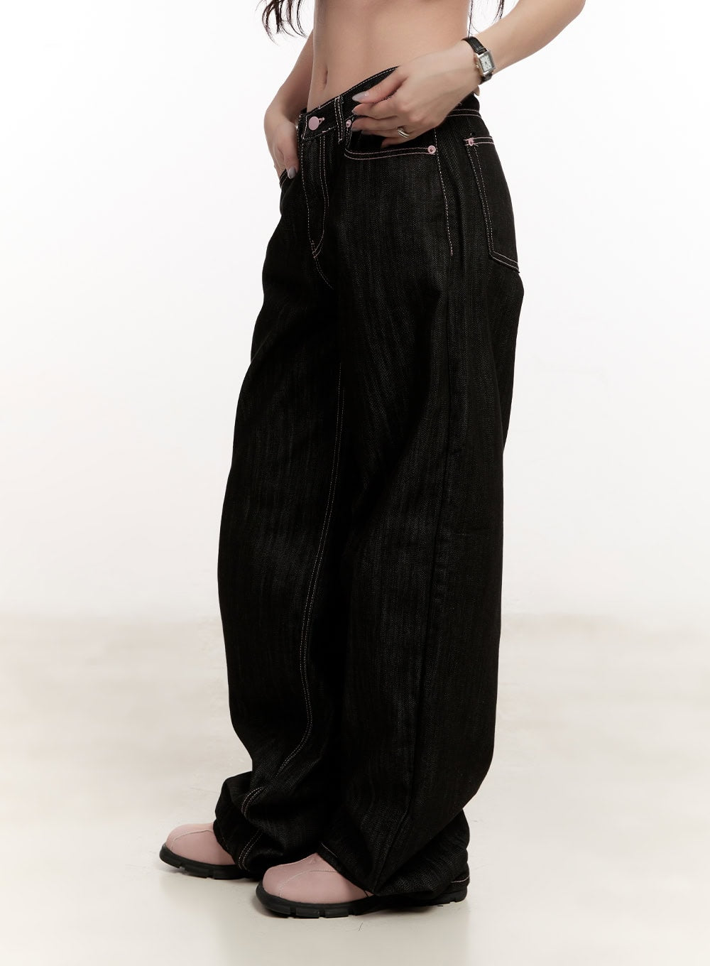 Trinity Stitched Baggy Jeans CM510 in black, side close-up on model, low-rise waistband with pink rivets and contrast stitch detail, voluminous wide leg silhouette.