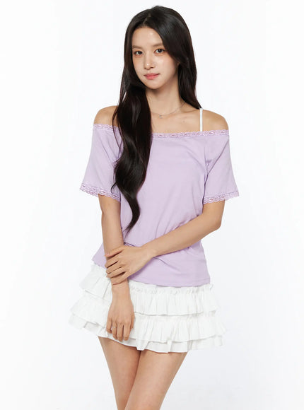 Lace Trim Off-Shoulder Tee CU522 in light purple, three-quarter front view on model, off-shoulder neckline with lace trim detail, relaxed fit, styled over white layered ruffle mini skirt.