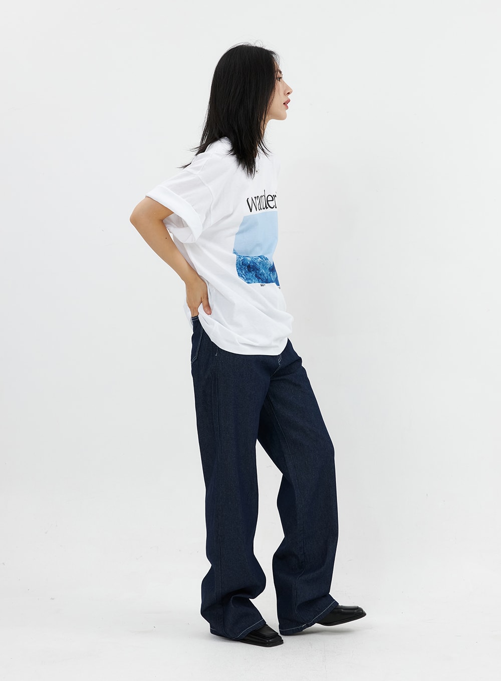 Stitched Jeans OO305 in Blue, three-quarter side view on model, wide-leg dark denim with contrast stitching, relaxed silhouette, paired with white graphic tee.