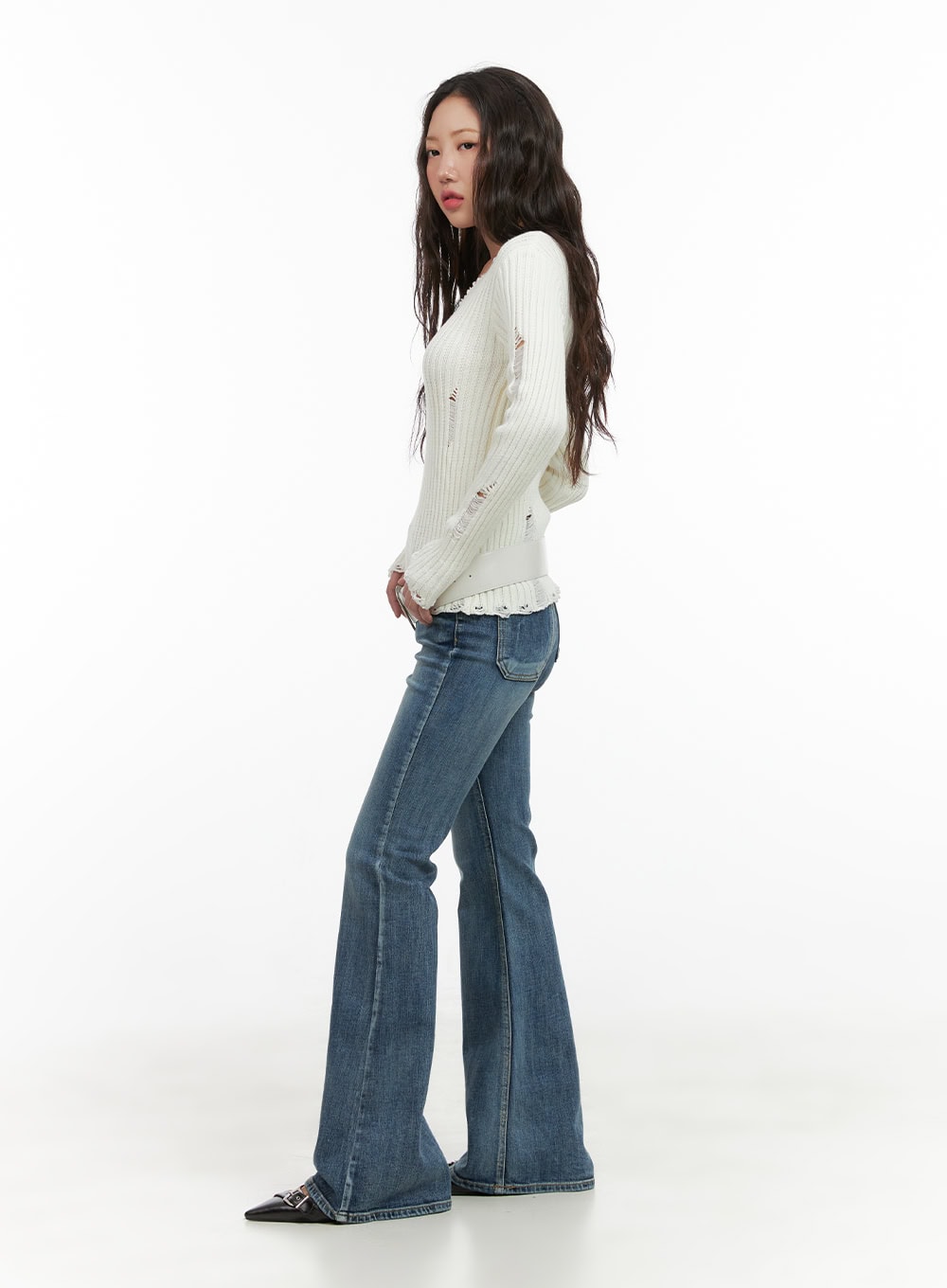 Lila Slim Bootcut Jeans CG422 in blue, full-body side shot on model looking back, slim fit washed denim with bootcut flare, styled with white distressed ribbed knit and black buckle flats.