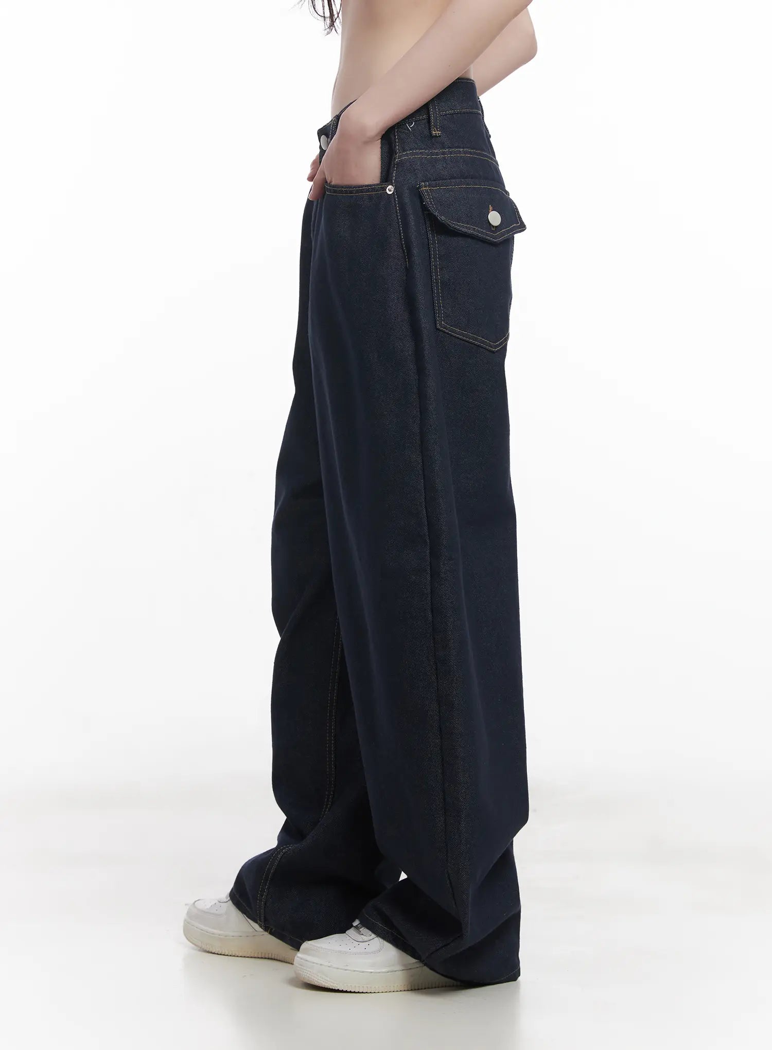 Hyein No-Fade Relaxed-Fit Jeans CU519 in dark blue, side close-up on model, showing flap pocket with snap button, contrast topstitching, and relaxed wide leg falling to sneakers.