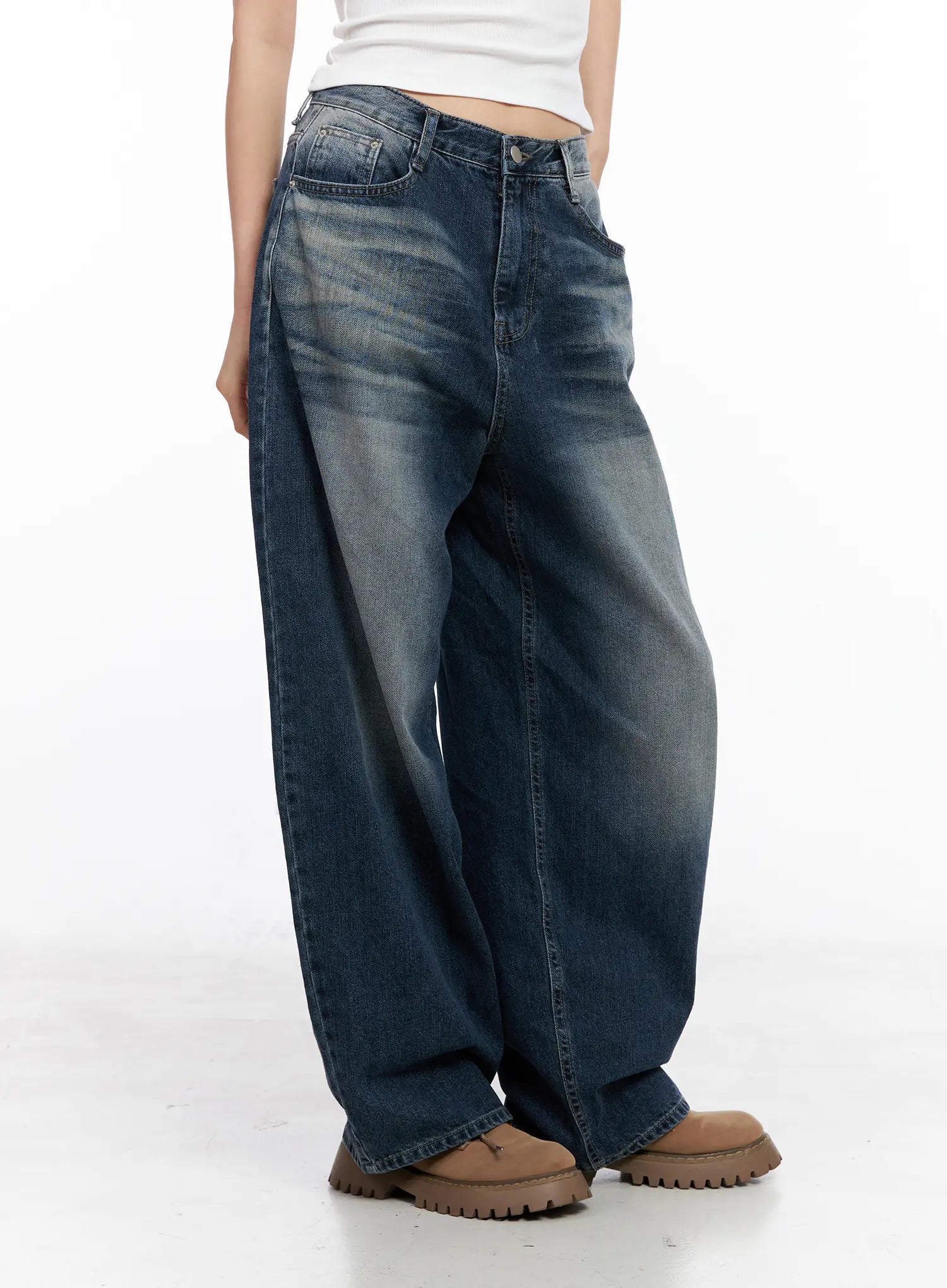 Aisha Washed Baggy Jeans CC1109 in mid blue, side view on model, highlighting baggy wide-fit silhouette, long length, washed fading along thigh, paired with white tank and chunky boots.